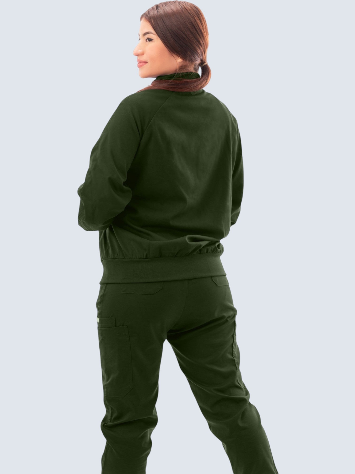 A woman wearing a dark green Kotyss scrub jacket with a high neck and ribbed cuffs, viewed from the back.