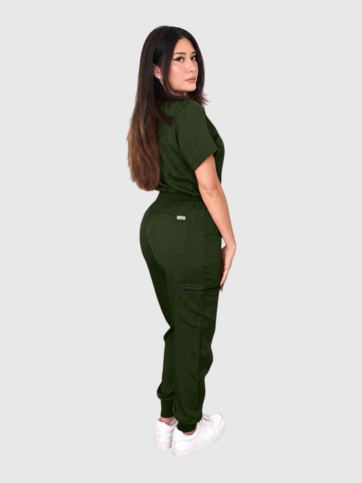 A woman wearing a dark green Kotyss V-neck scrub top and multi-pocket jogger pants, side view.