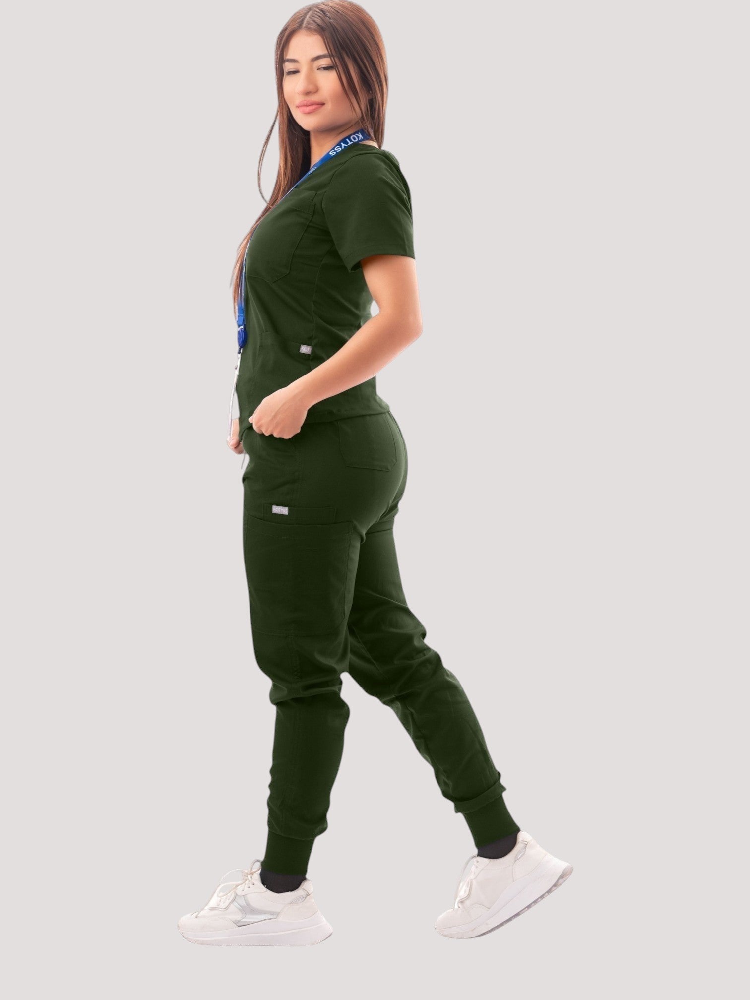 Woman wearing a dark green Kotyss V-neck scrub top and jogger pants set with multiple pockets.