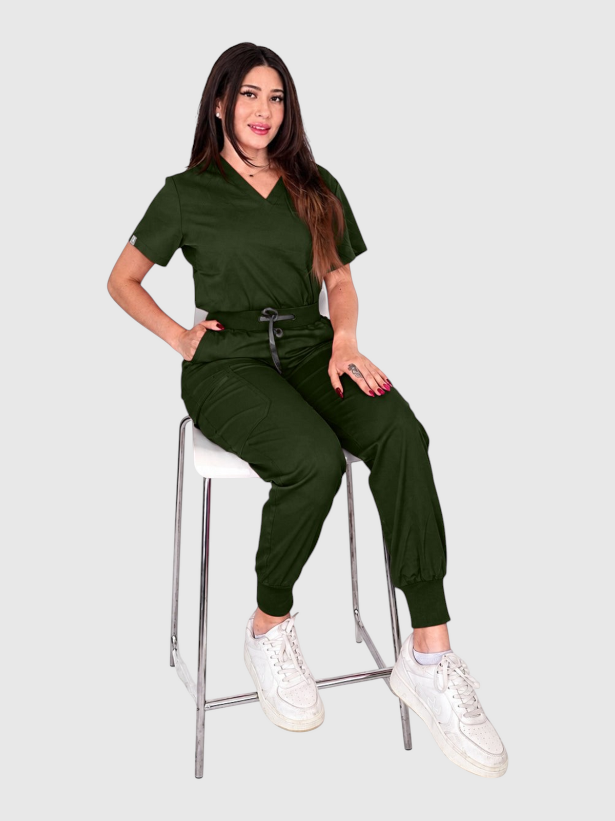 Kotyss women's dark green V-neck scrub top and jogger pants set with multiple pockets on a model sitting on a stool.