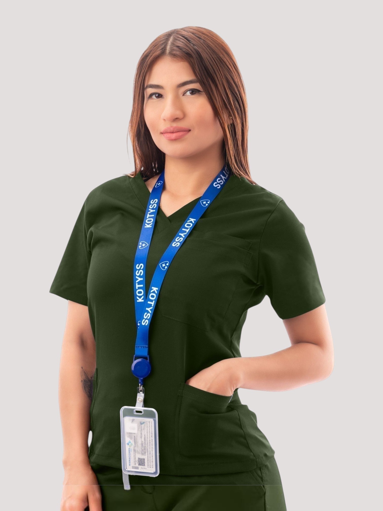 A woman wearing a dark green Kotyss V-neck medical scrub top with pockets and a blue branded lanyard.