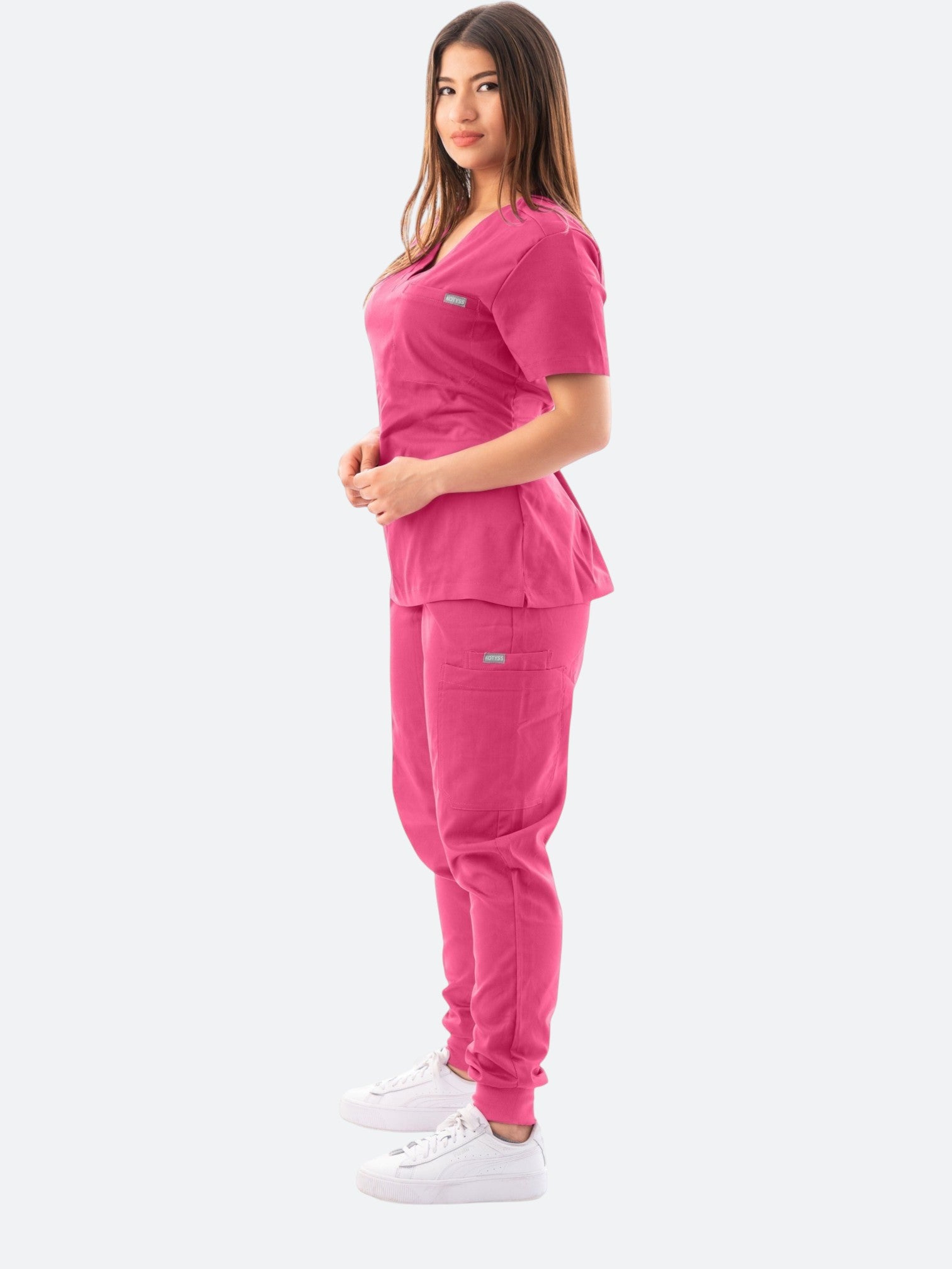 A woman wearing a Kotyss fuchsia pink V-neck scrub top and jogger pants set with multiple pockets.