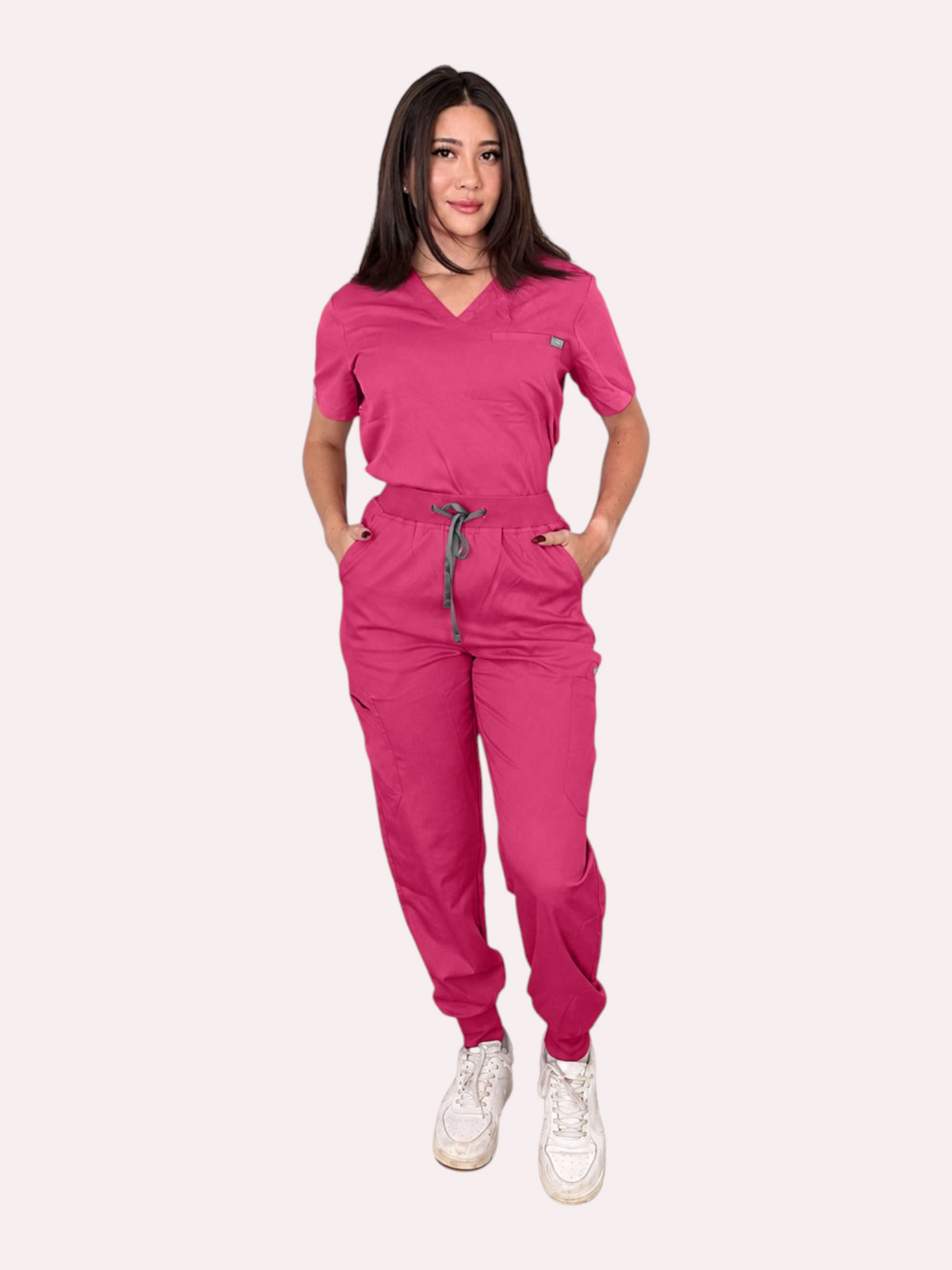 A woman wearing a Kotyss fuchsia V-neck scrub top and matching multi-pocket jogger pants with a drawstring waist.