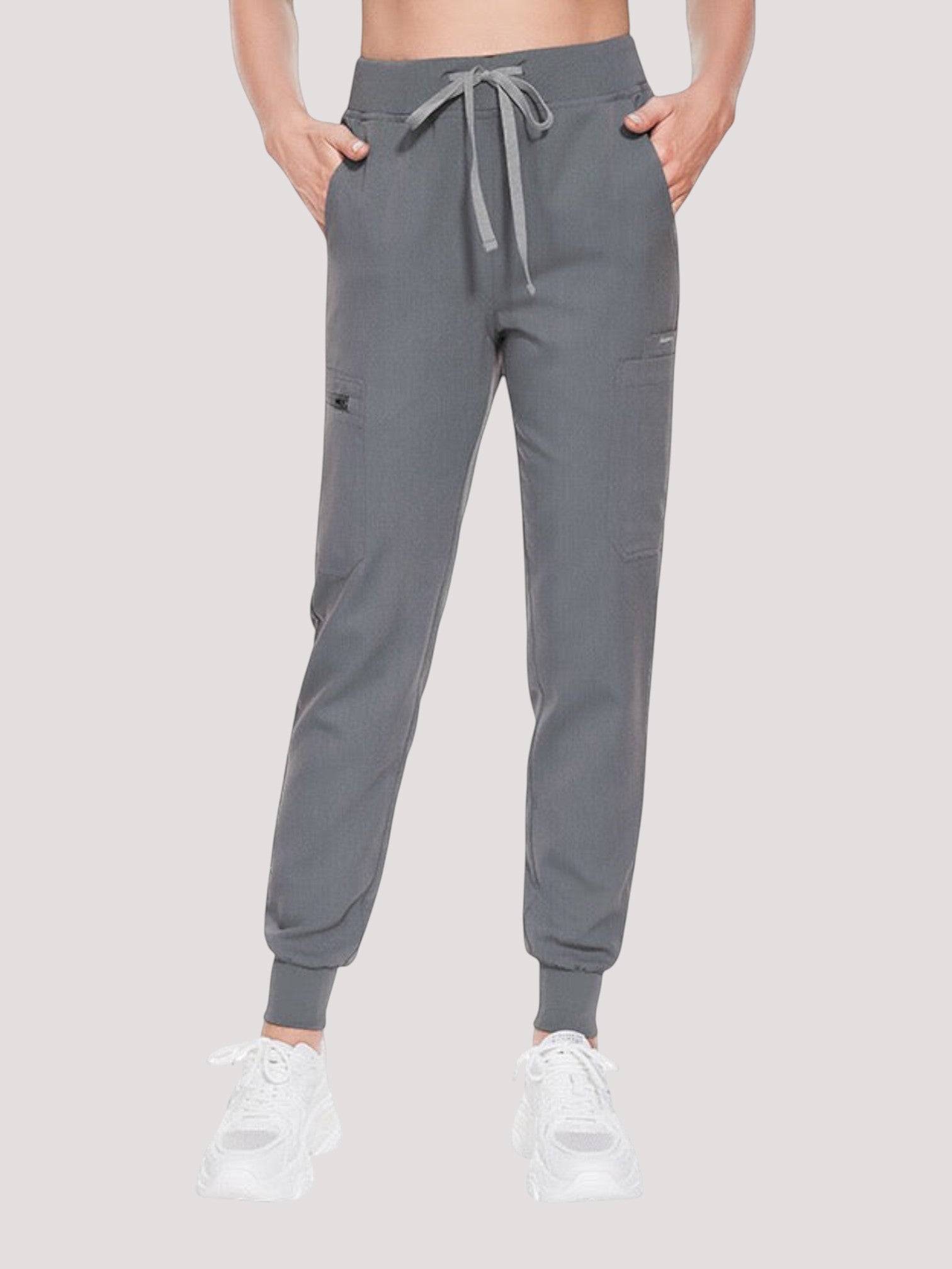 Kotyss grey medical scrub jogger pants with a drawstring waist and multiple pockets on a model wearing white sneakers
