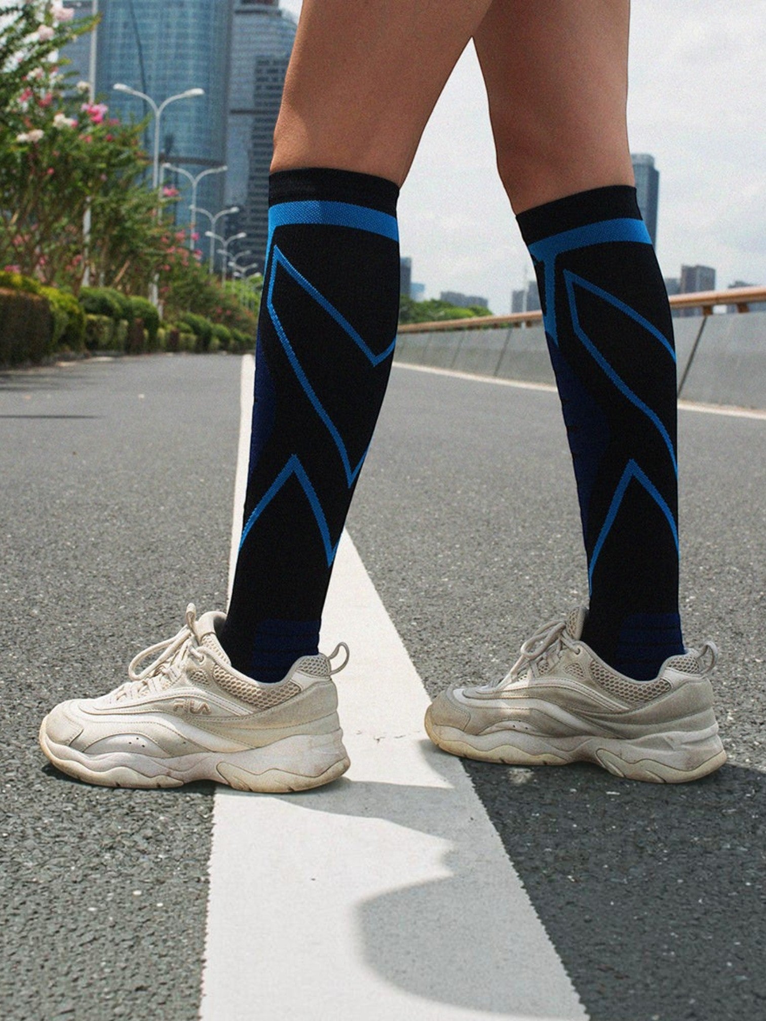 Kotyss knee high compression socks in black and blue with geometric patterns worn by a person on an outdoor road