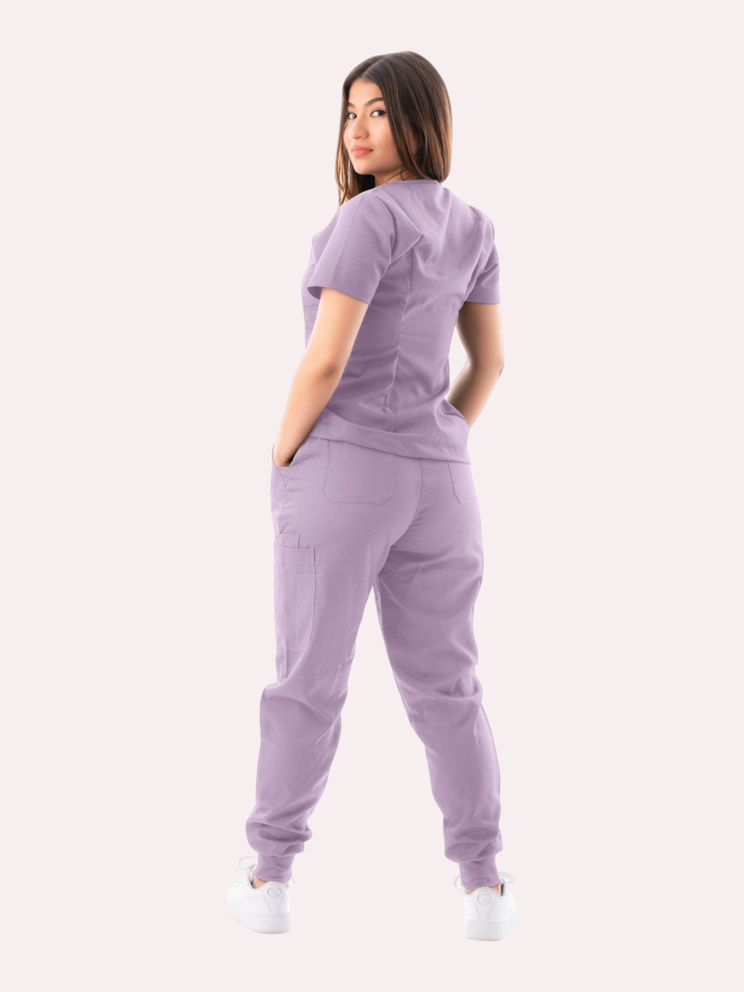 Woman wearing a lavender Kotyss V-neck scrub top and jogger pants set, back view showing multiple utility pockets.