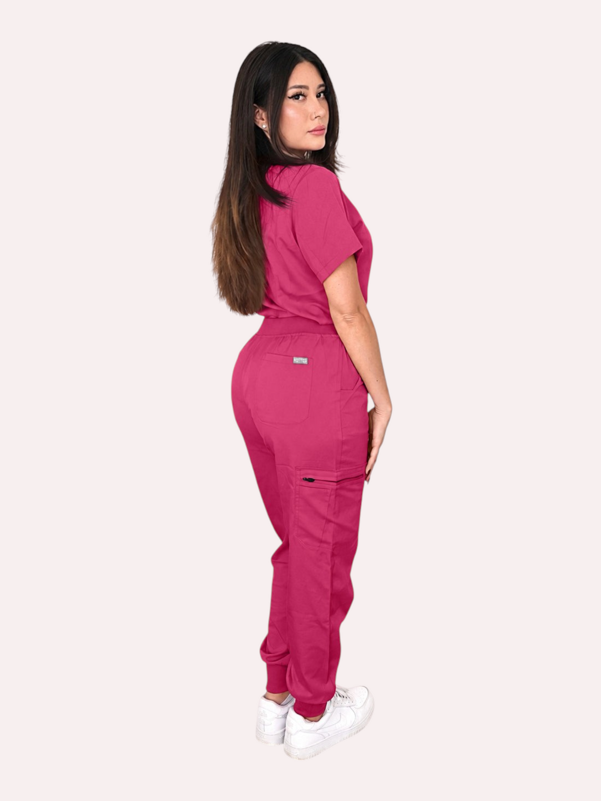 A model wearing a Kotyss magenta V-neck scrub top and multi-pocket jogger pants set with a side view.