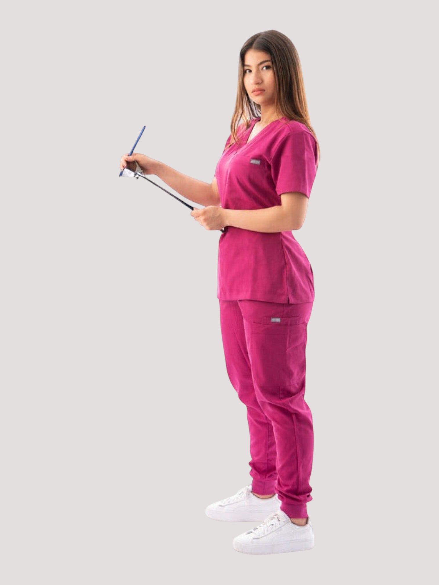 Kotyss women's magenta V-neck scrub top and jogger pants set with multiple pockets on a female model holding a clipboard