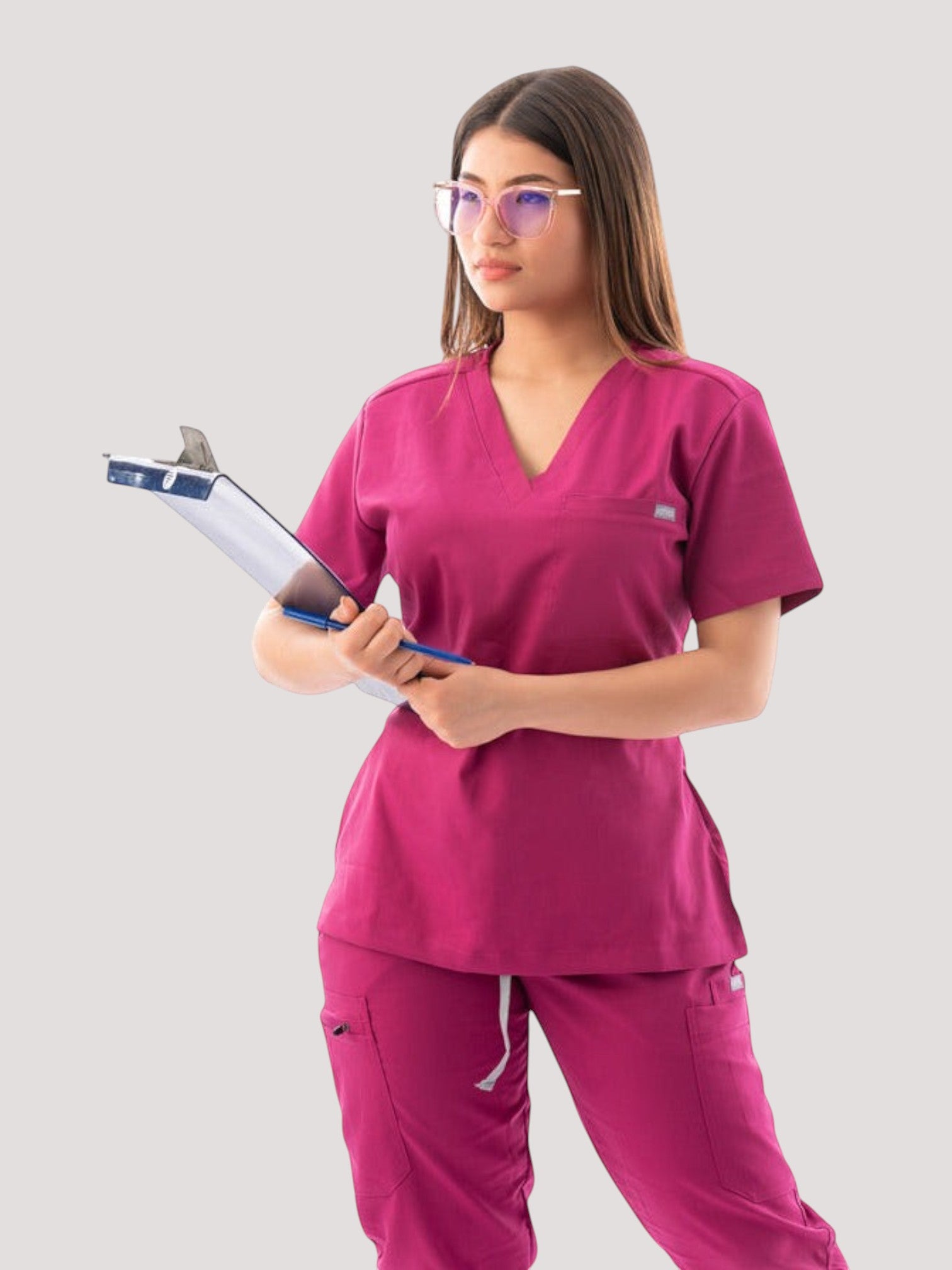 A woman wearing a magenta Kotyss V-neck scrub top and matching jogger pants, holding a clipboard.