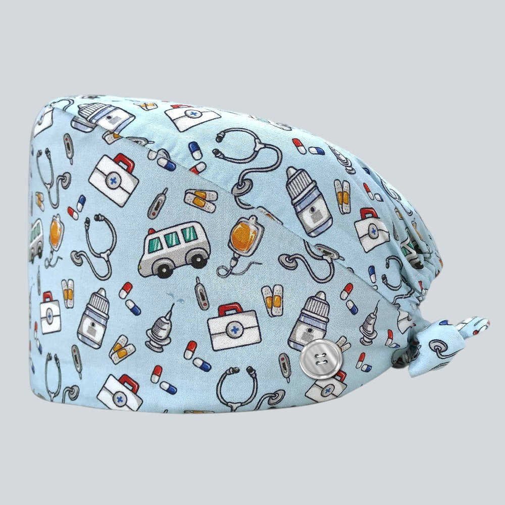 Kotyss light blue scrub cap with medical print featuring ambulances, stethoscopes, and pills with side buttons.
