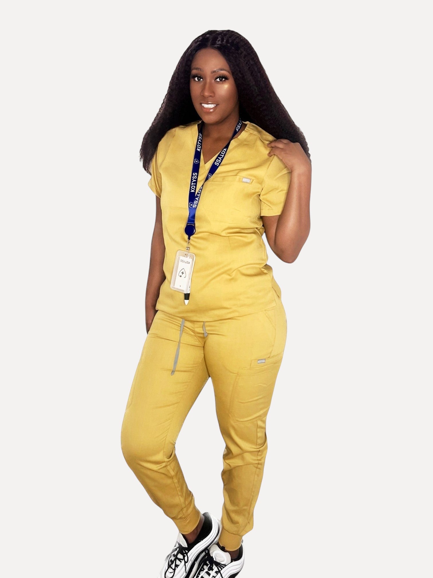 Model wearing a mustard yellow Kotyss V-neck scrub top and jogger pants set with multiple pockets and 4-way stretch.