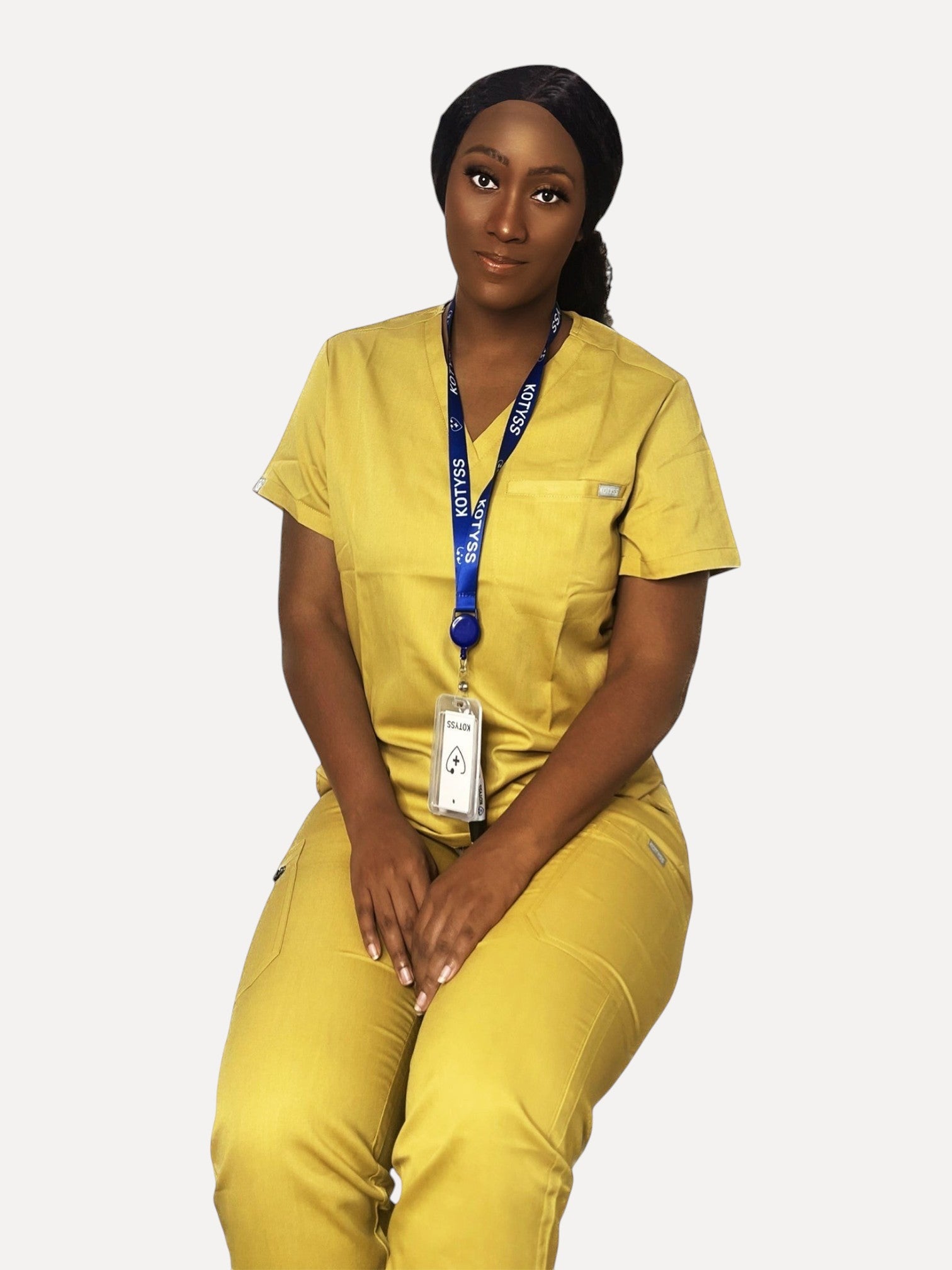 A woman wearing a mustard yellow Kotyss V-neck scrub top and matching jogger pants with a branded lanyard.