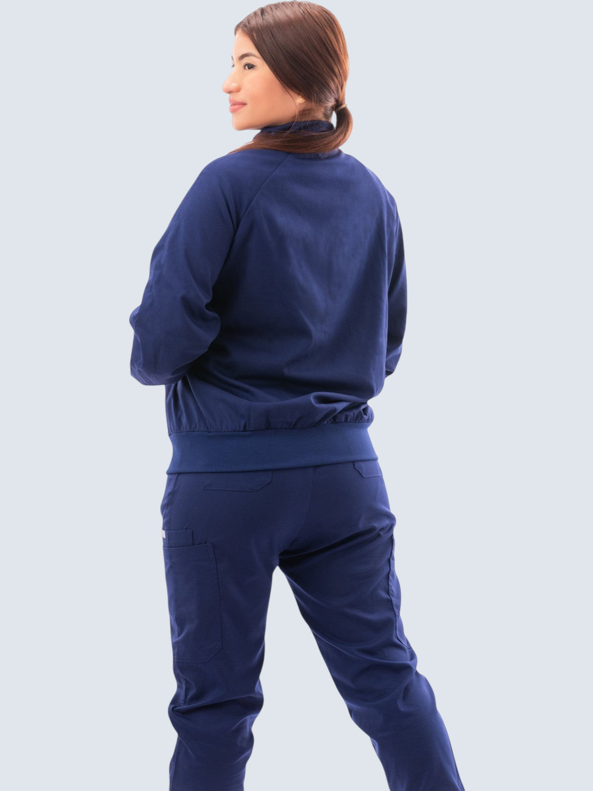 Kotyss women's navy blue scrub jacket with a high neck and ribbed cuffs, shown from the back on a healthcare worker.