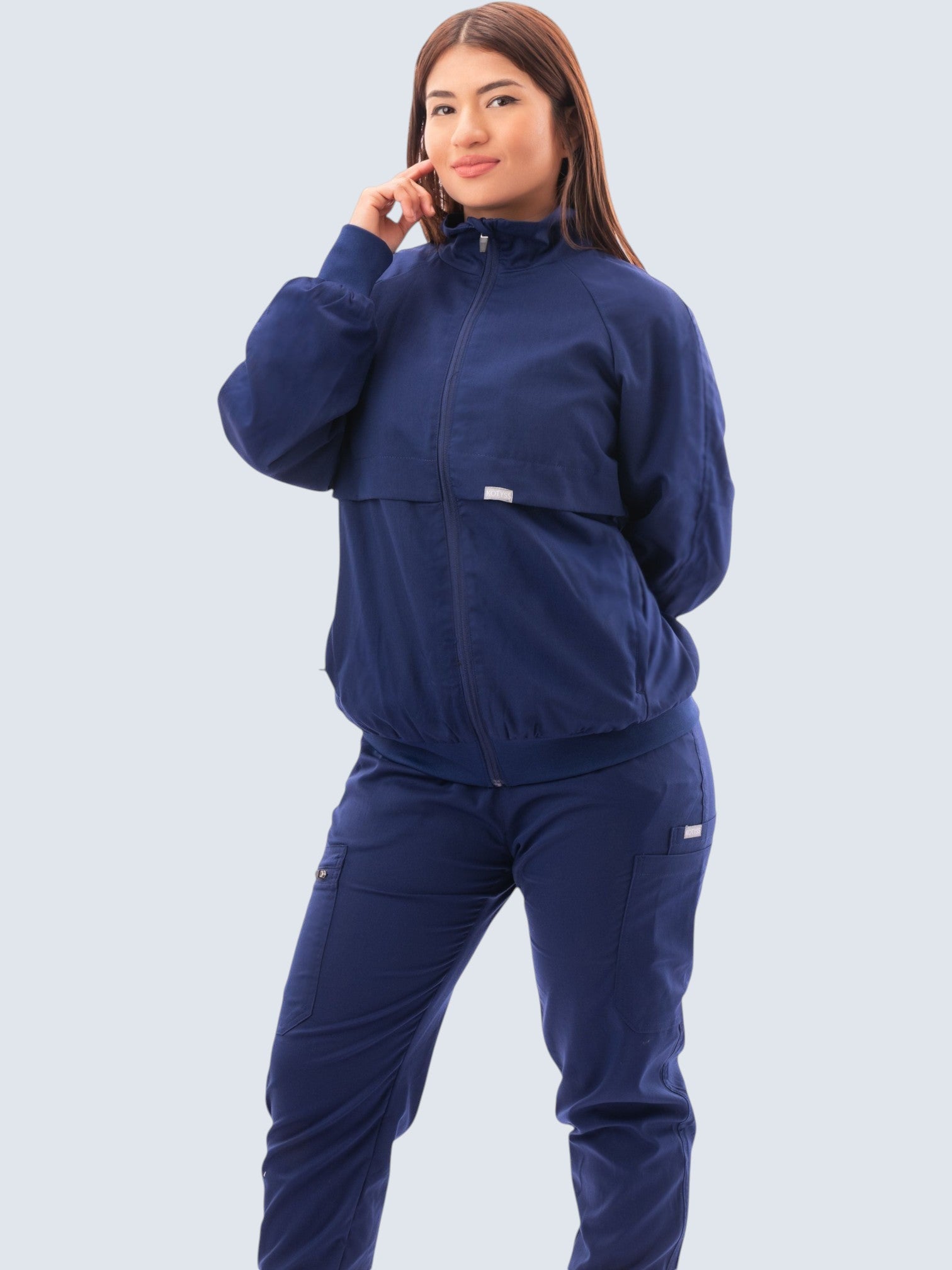 A woman wearing a navy blue Kotyss scrub jacket with a high windbreaker neck, ribbed cuffs, and a tailored fit.