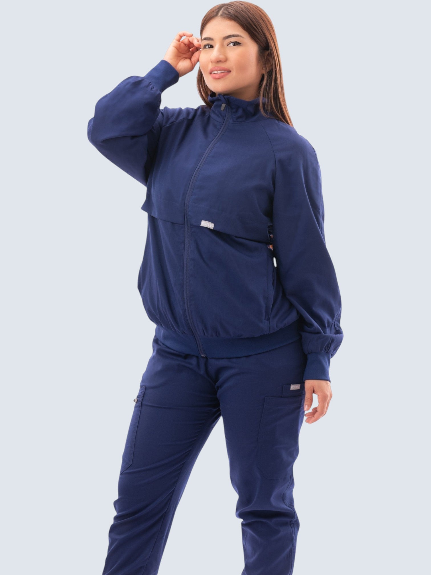 A woman wearing a navy blue Kotyss scrub jacket with a high neck, zip front, and ribbed cuffs for a professional look.