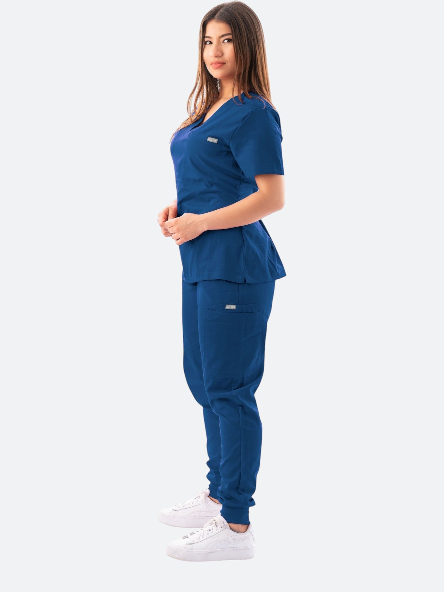 A woman wearing a navy blue Kotyss V-neck scrub top and matching jogger pants with multiple pockets.