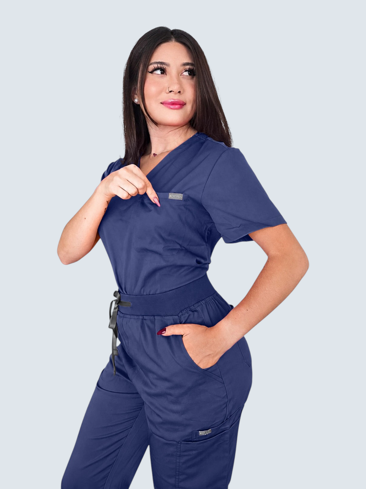 A woman wearing a navy blue Kotyss V-neck scrub top and jogger pants set with multiple pockets.