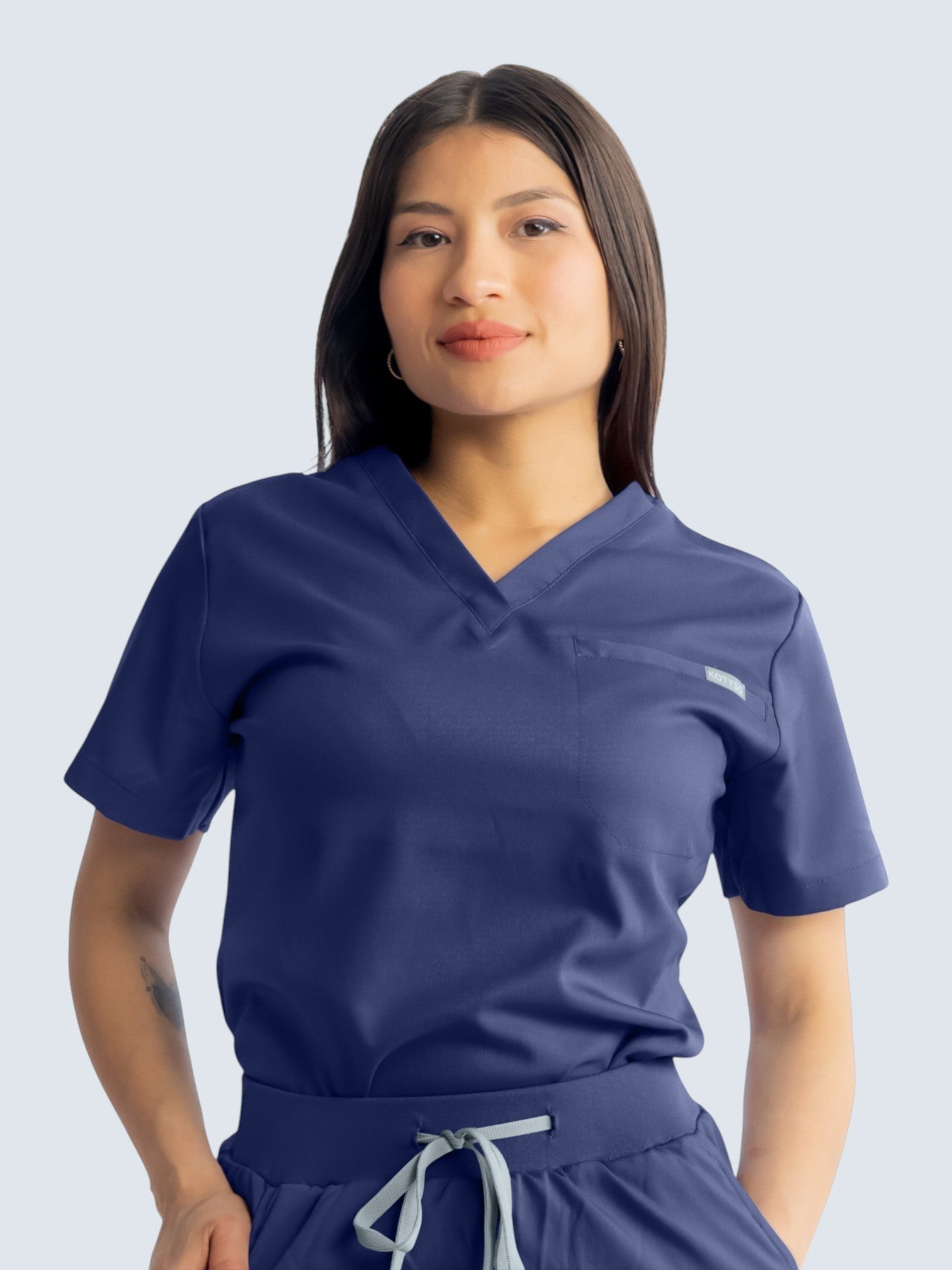 A model wearing Kotyss navy blue medical scrub top with a V-neck and chest pocket, made of soft, breathable fabric.