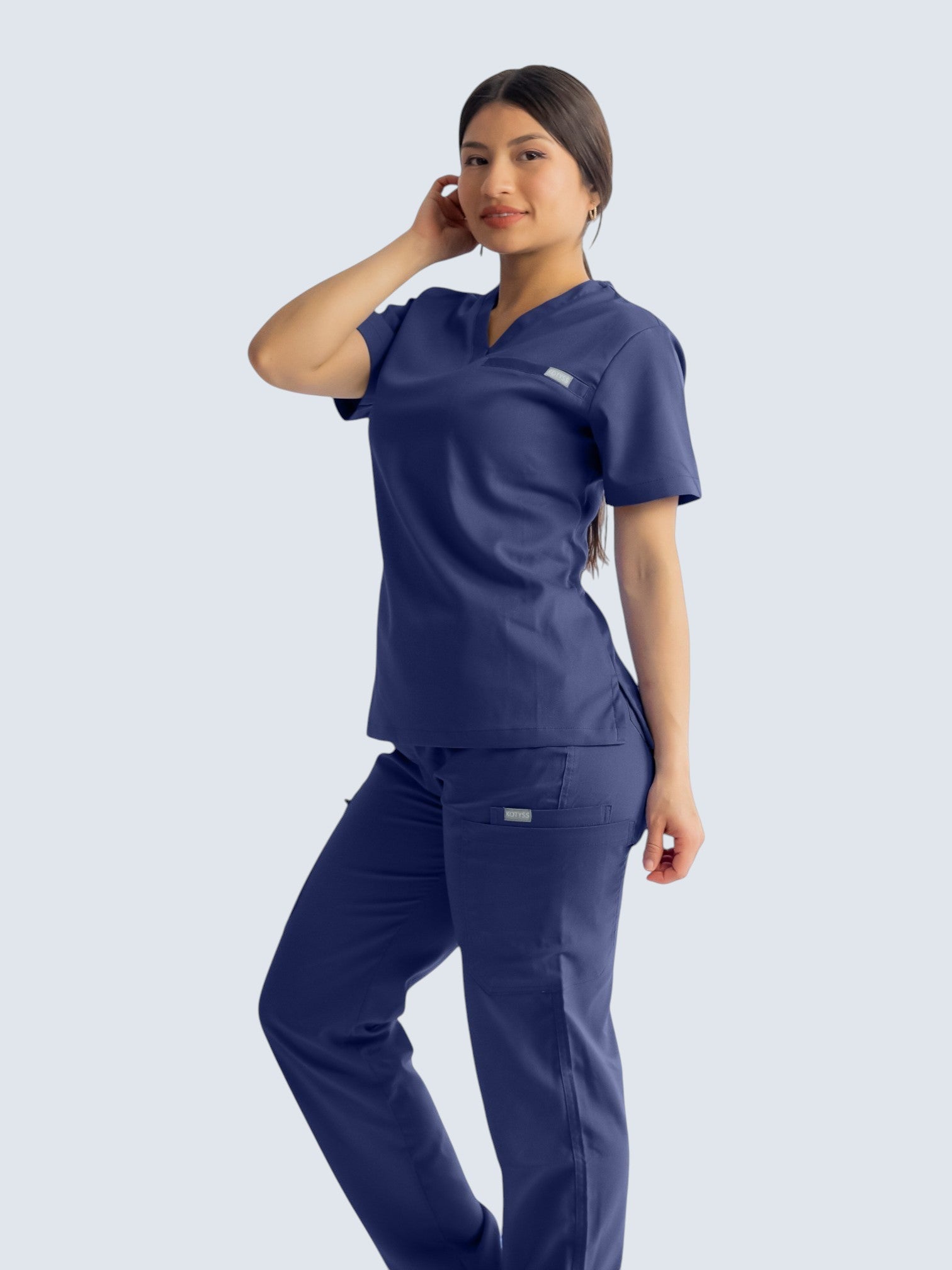 A woman wearing Kotyss navy blue straight cut medical scrub pants and matching top with multiple utility pockets.