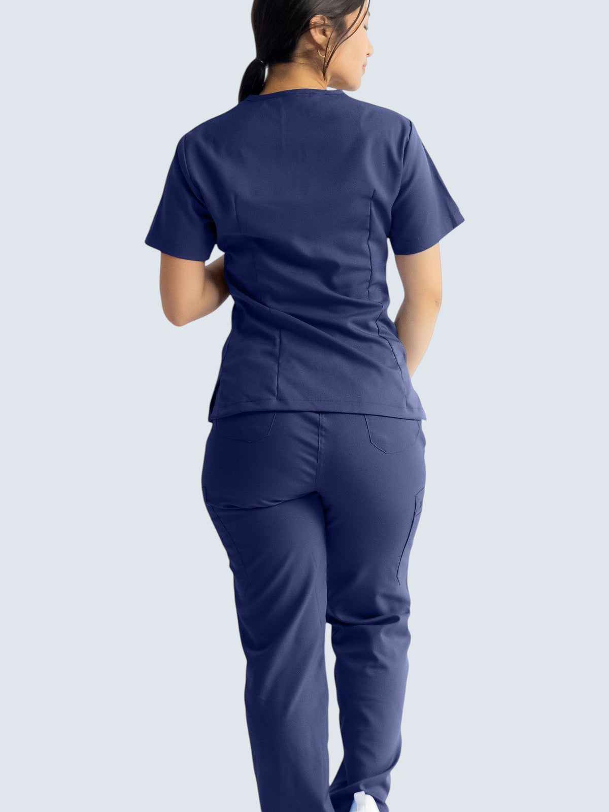 A woman wearing Kotyss navy blue straight cut medical scrub pants and matching top, seen from the back.