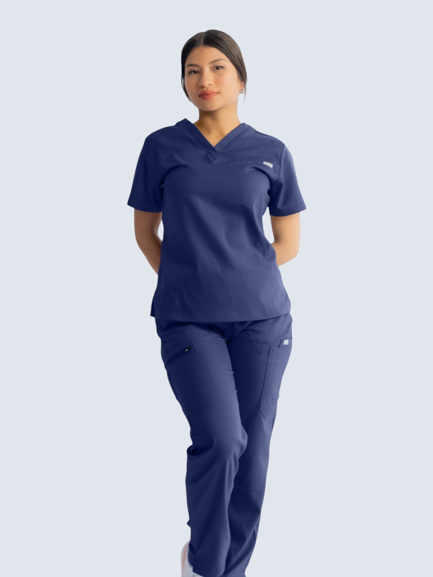 A healthcare professional wearing Kotyss navy blue straight cut scrub pants and a matching V-neck scrub top.