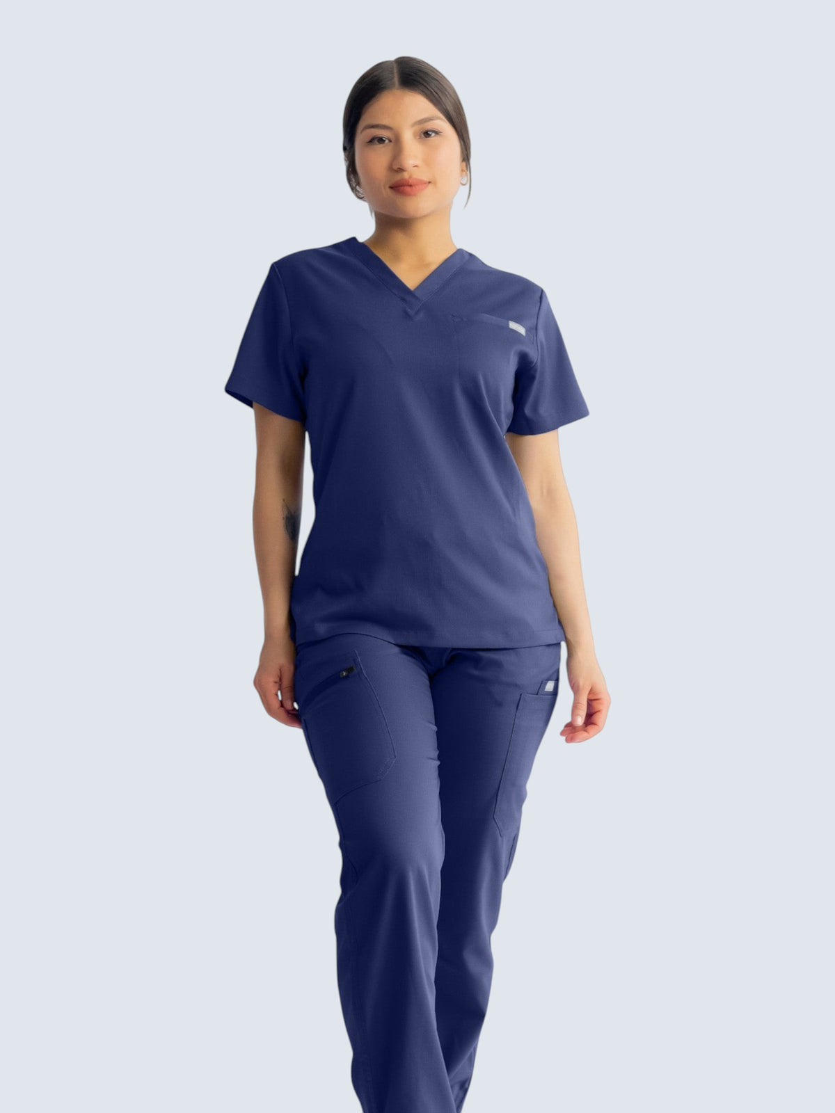 A model wearing Kotyss navy blue straight cut medical scrub pants and matching v-neck top with multiple pockets.