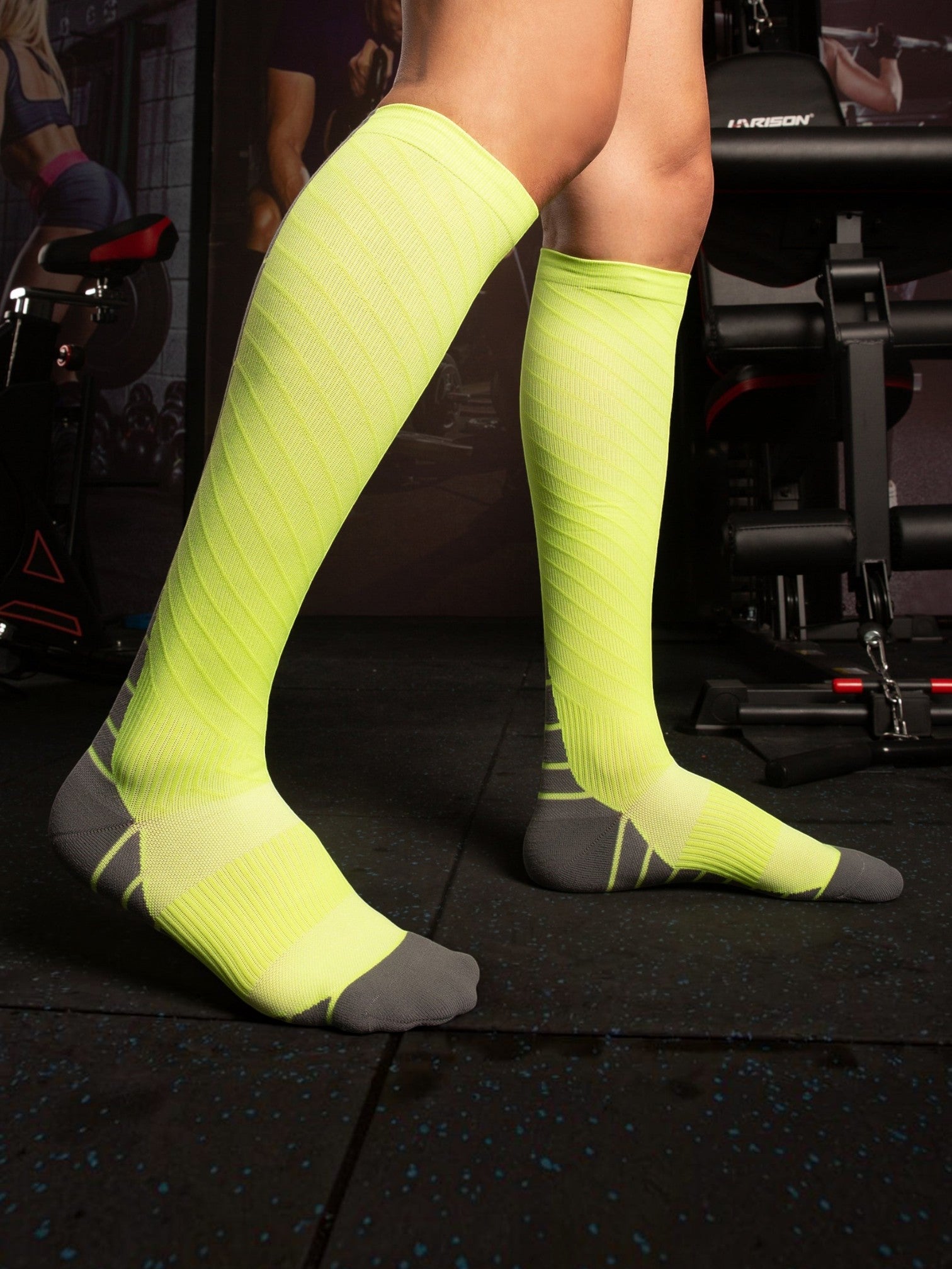 Kotyss neon yellow and grey knee-high compression socks with seamless design worn by a person in a gym setting