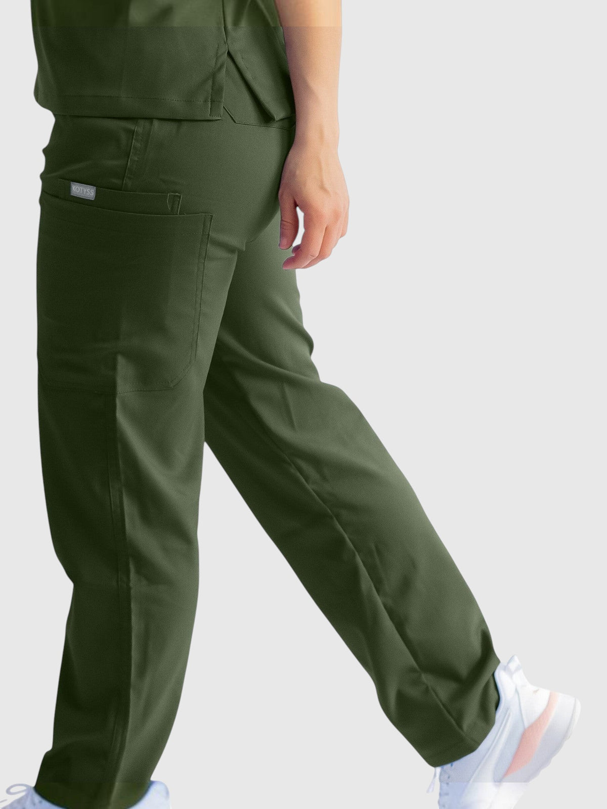 Kotyss olive green straight cut medical scrub pants with multiple pockets on a model wearing white sneakers