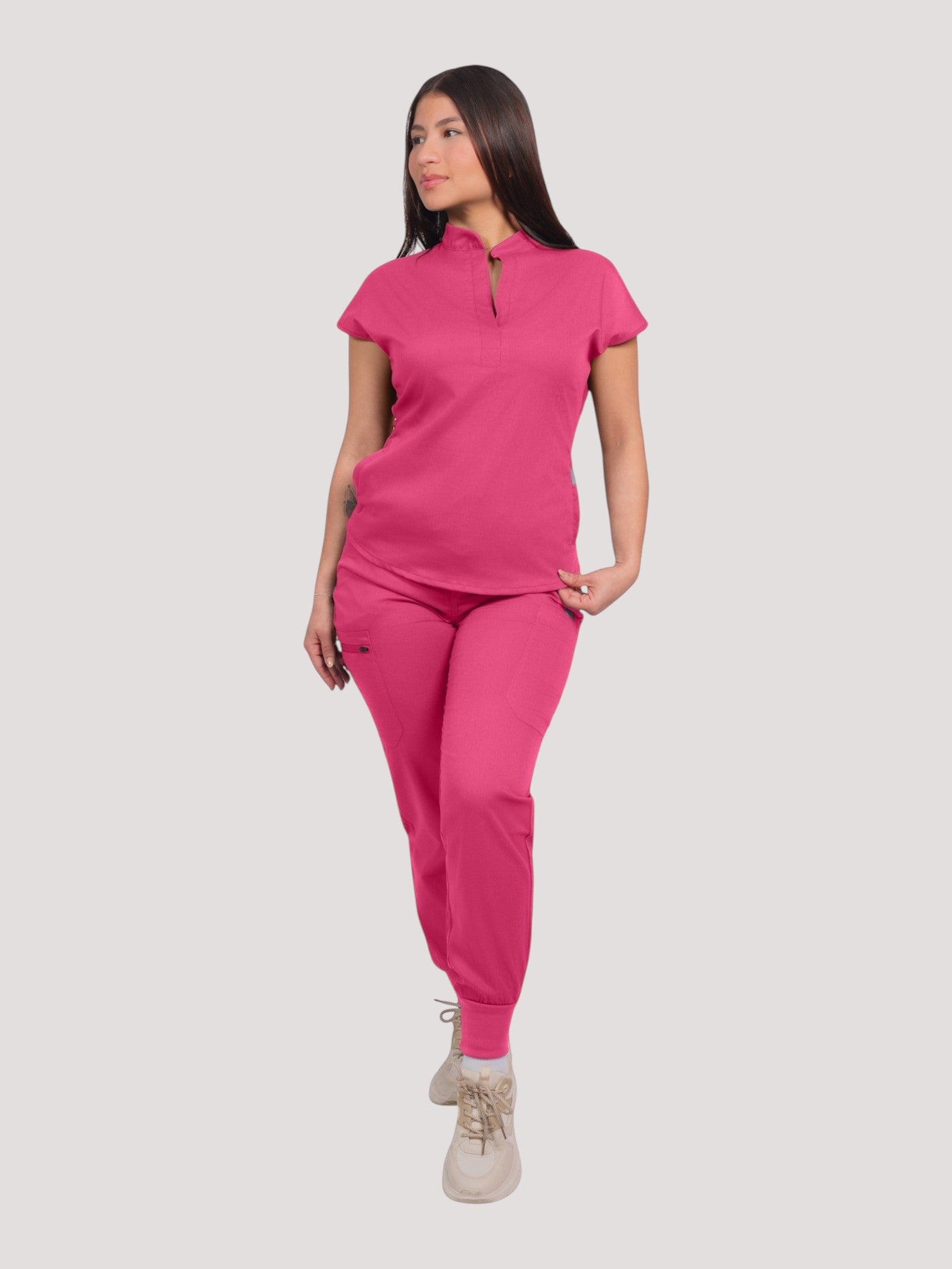 A model wearing a bright pink Kotyss collared scrub top and matching jogger pants with multiple pockets.