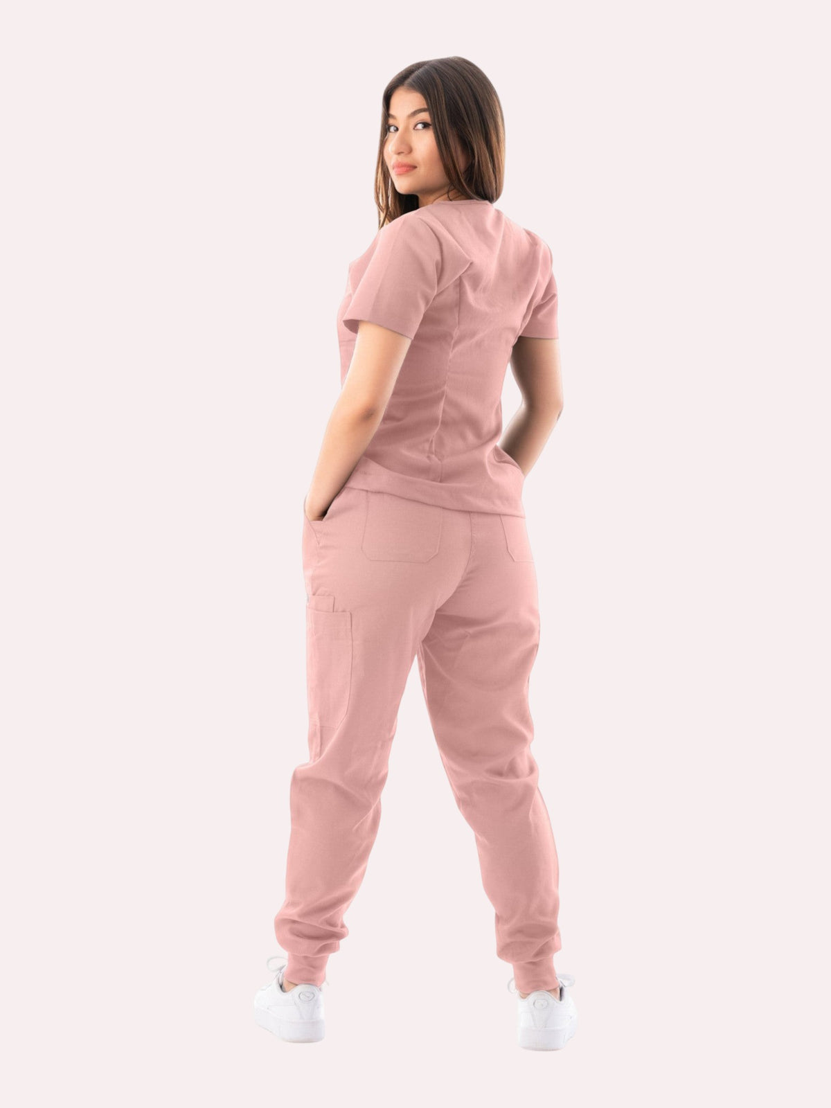 A woman wearing a dusty pink Kotyss V-neck scrub top and jogger pants set, viewed from behind.