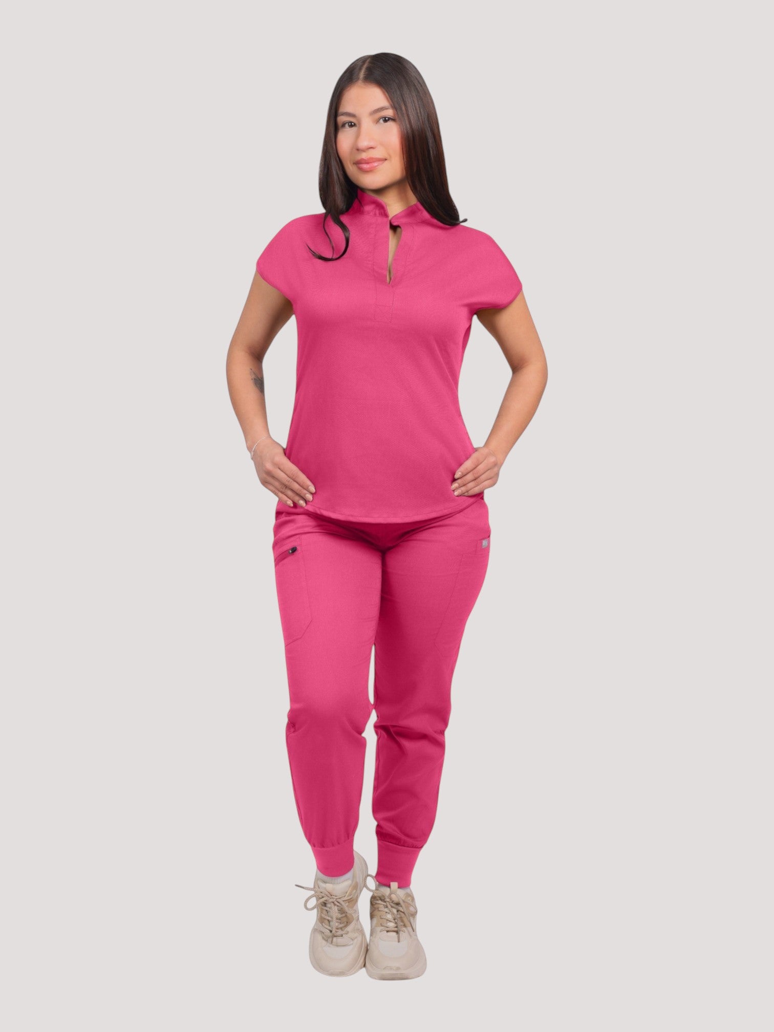 A woman wearing a vibrant pink Kotyss collared scrub top and matching jogger pants with multiple pockets.