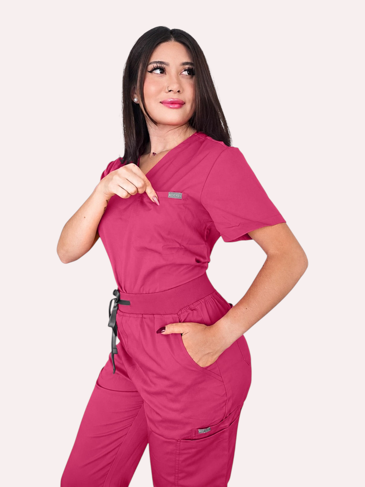 A woman wearing a vibrant pink Kotyss V-neck scrub top and matching jogger pants with multiple utility pockets.
