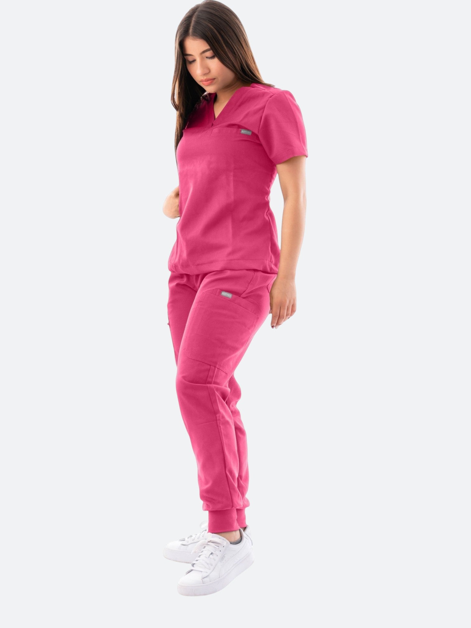A woman wearing a vibrant pink Kotyss V-neck scrub top and matching jogger pants with multiple pockets.
