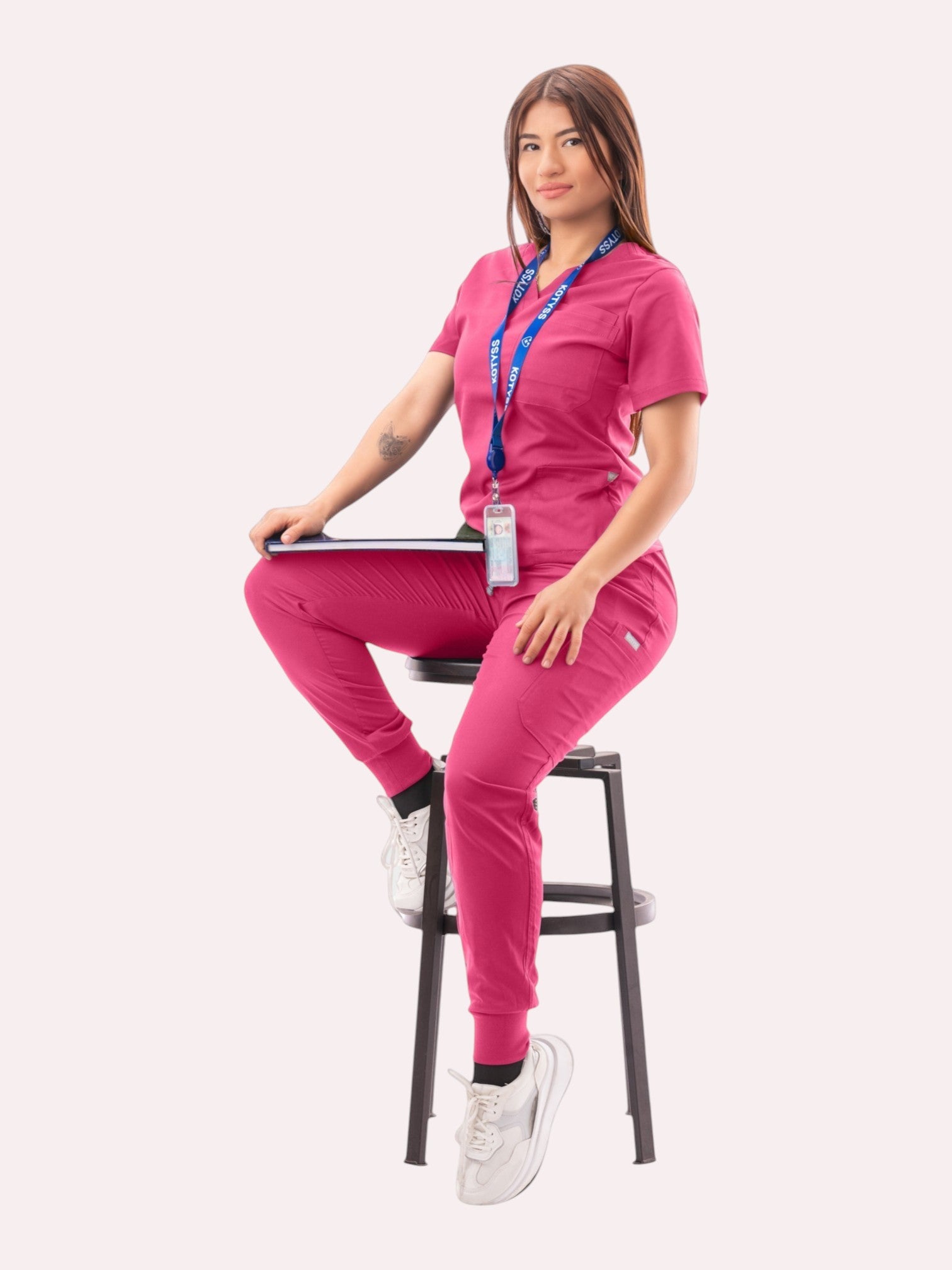 Kotyss women's pink V-neck scrub top and jogger pants set with multi-pocket design worn by a seated model