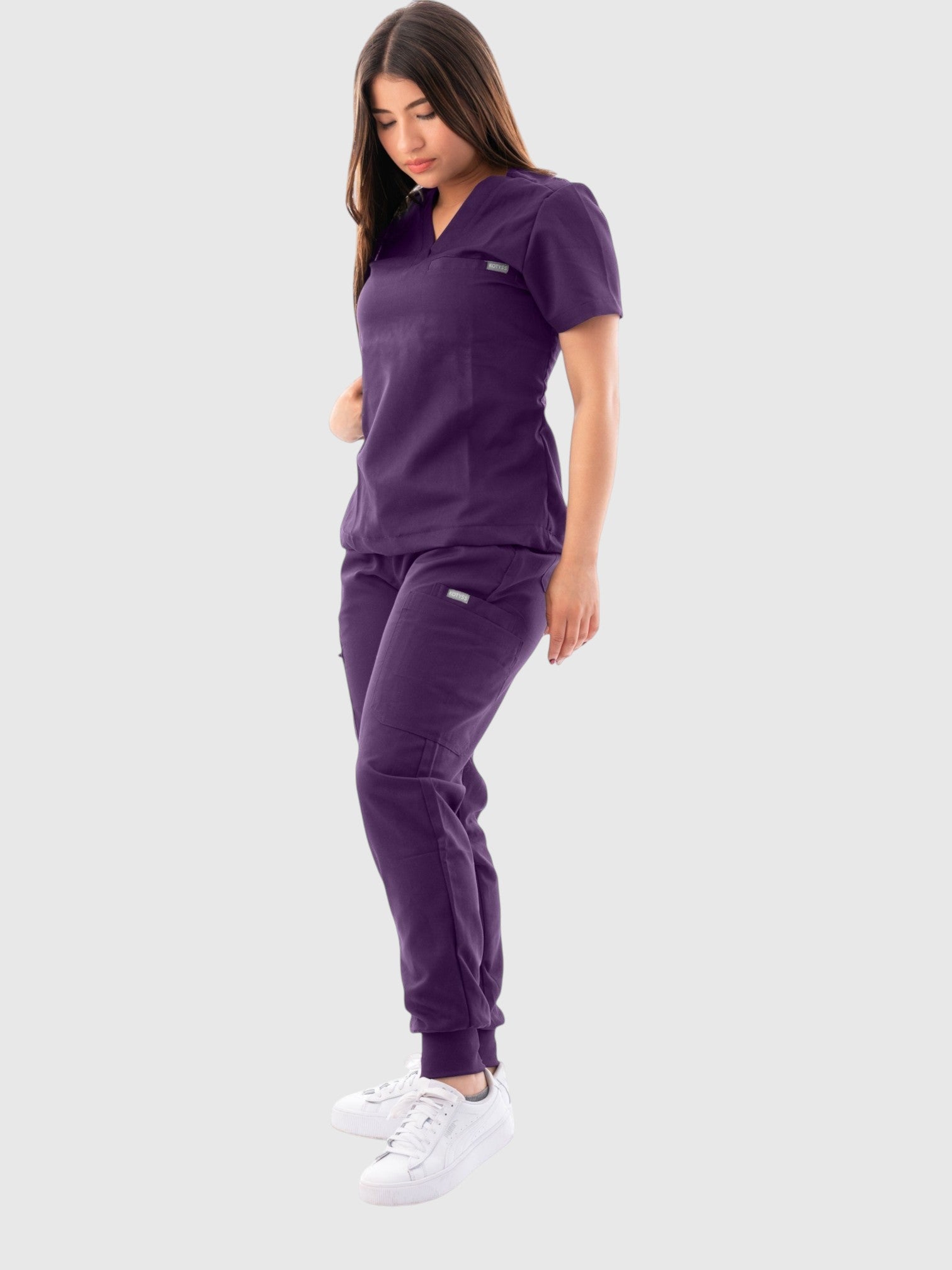 Kotyss women's deep purple V-neck scrub top and jogger pants set with multiple pockets on a model.