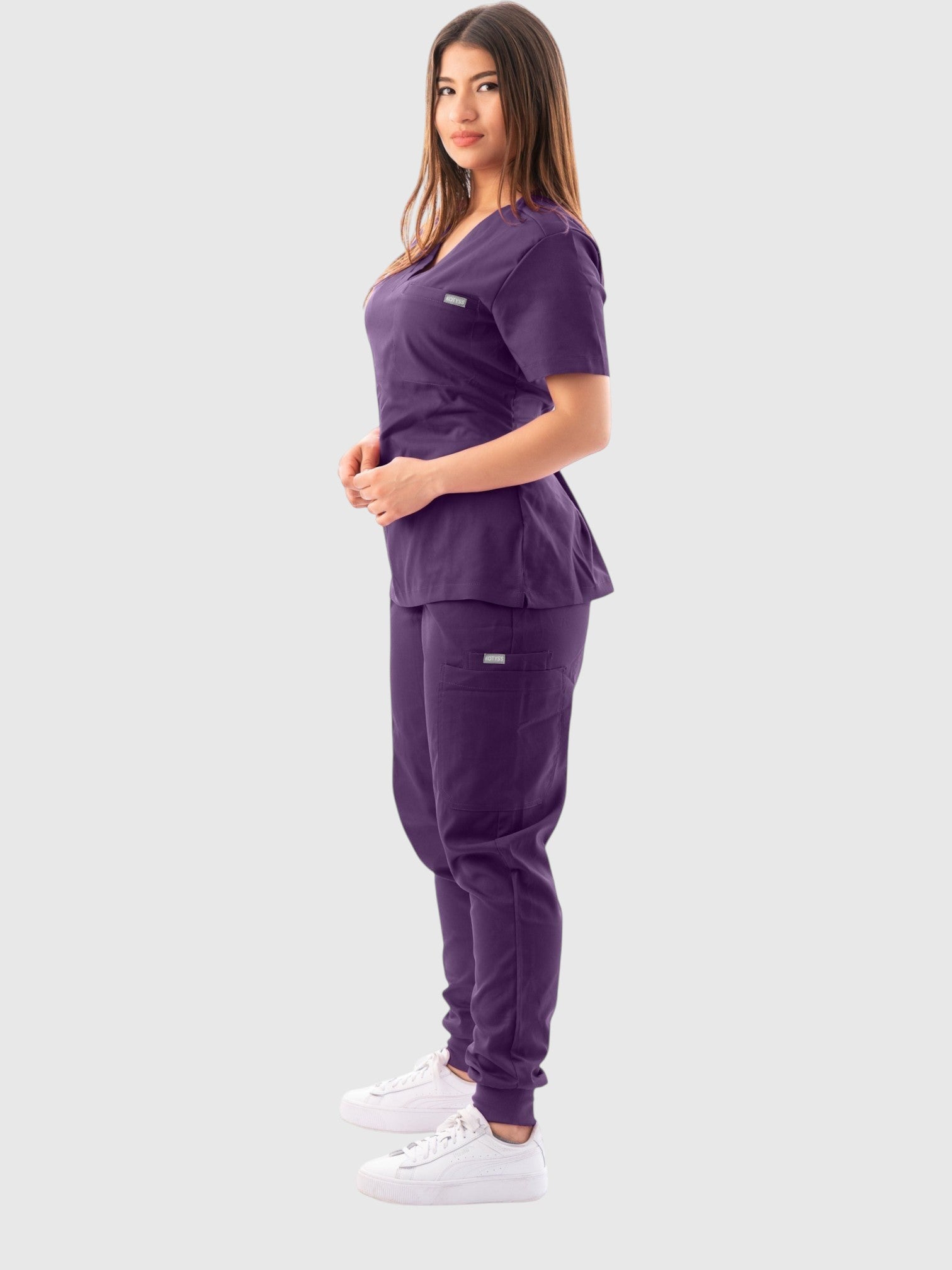Woman wearing a purple Kotyss V-neck scrub top and jogger pants set with multiple pockets, side view.
