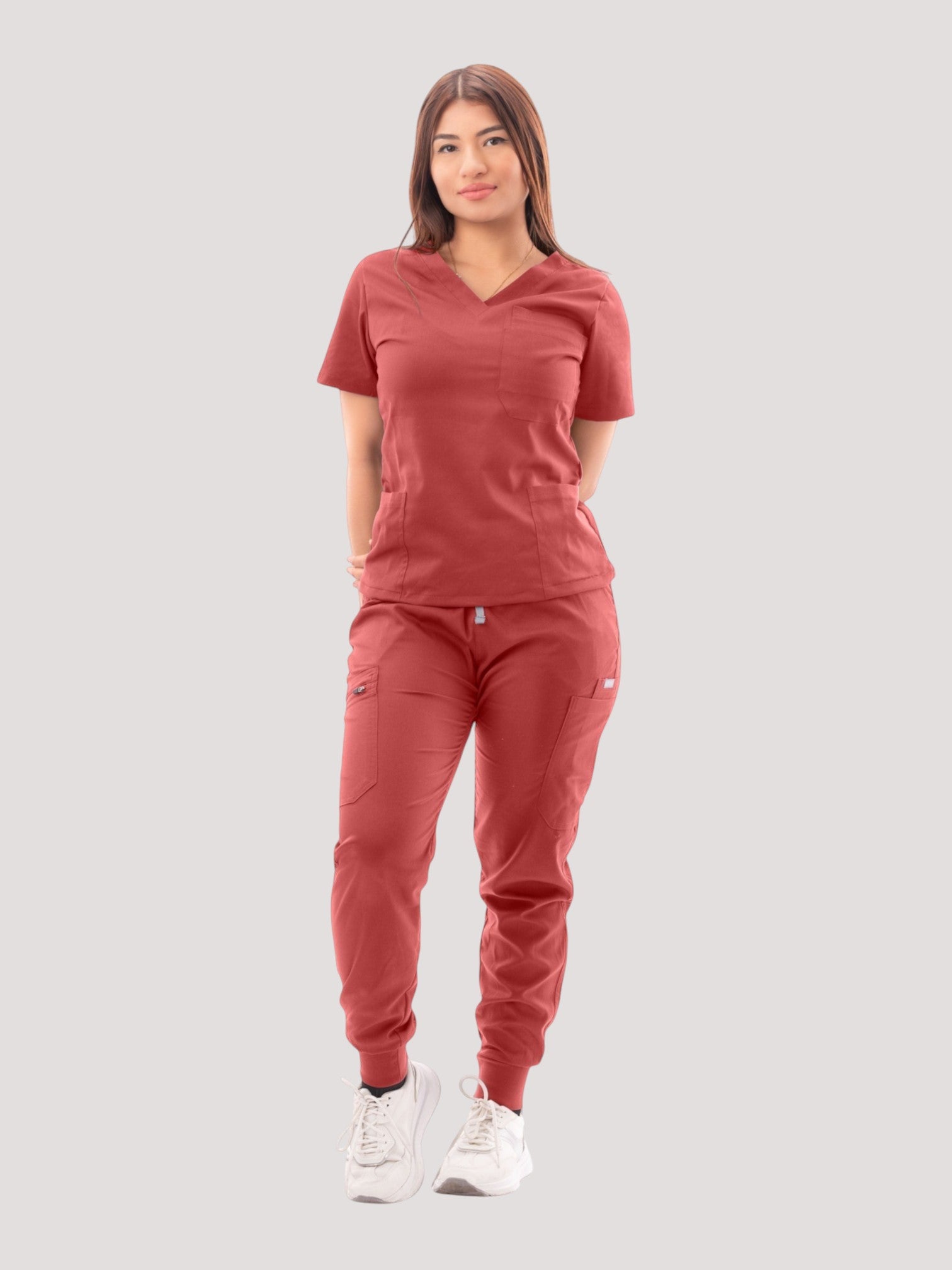 A woman wearing a Kotyss red V-neck scrub top and matching multi-pocket jogger pants with white sneakers.