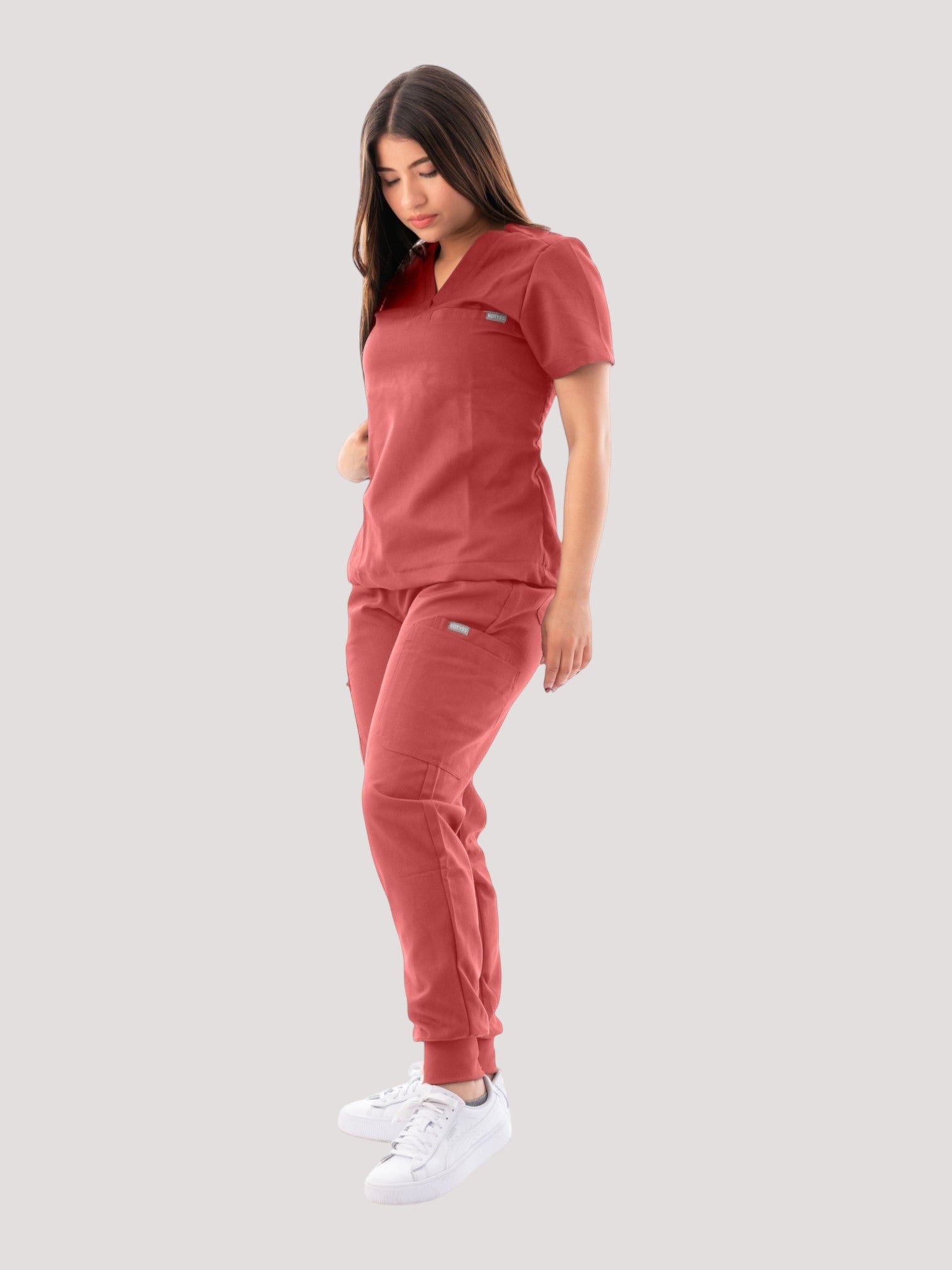 Woman wearing a red Kotyss V-neck scrub top and jogger pants set with multiple pockets, isolated on white background