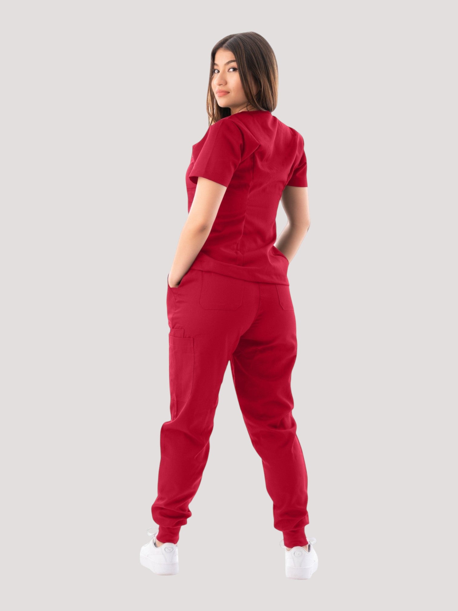 Model wearing a red Kotyss V-neck scrub top and jogger pants set, featuring multiple pockets and a slim fit.