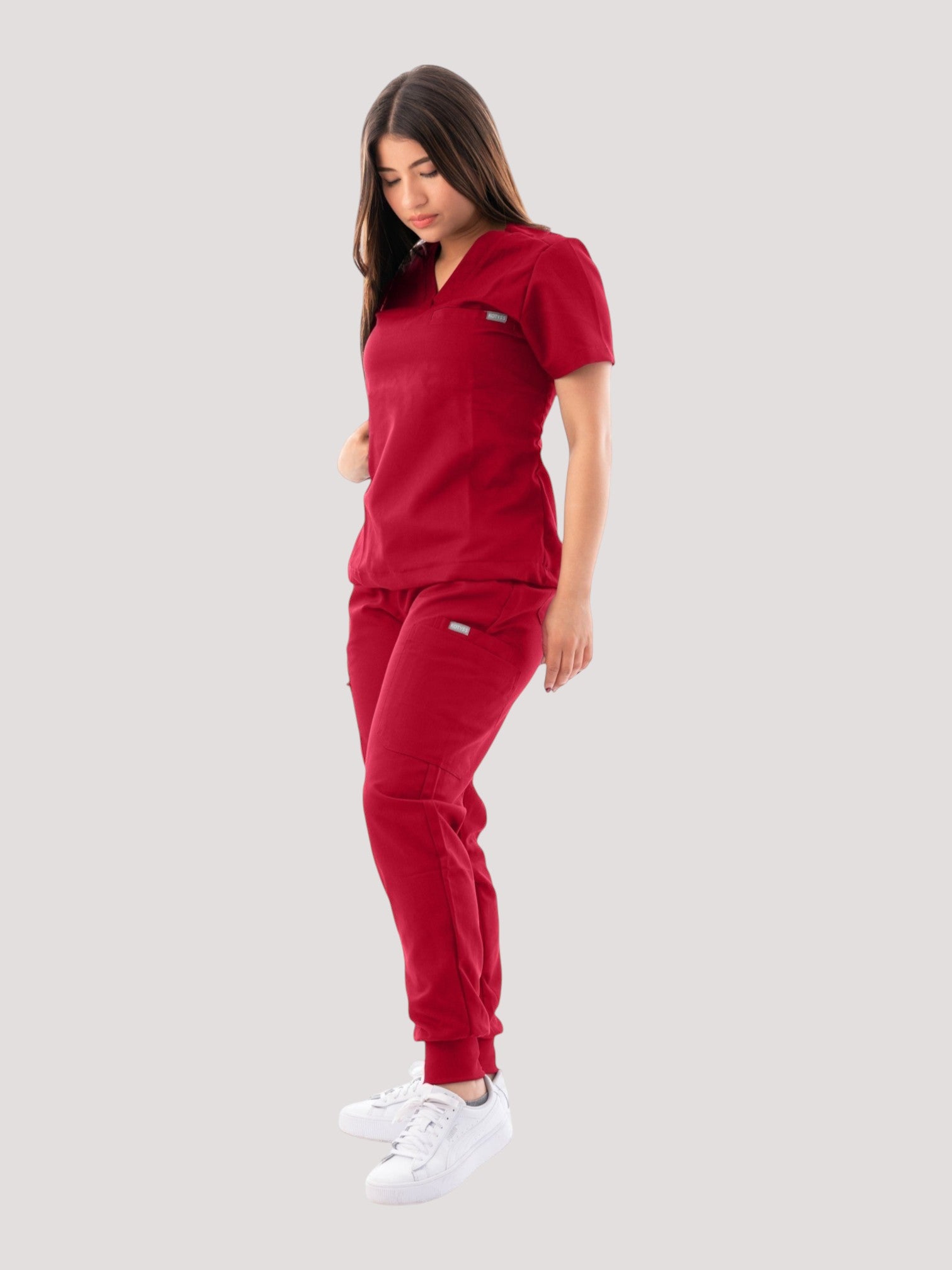 A woman wearing a red Kotyss V-neck scrub top and matching jogger pants with multiple pockets.