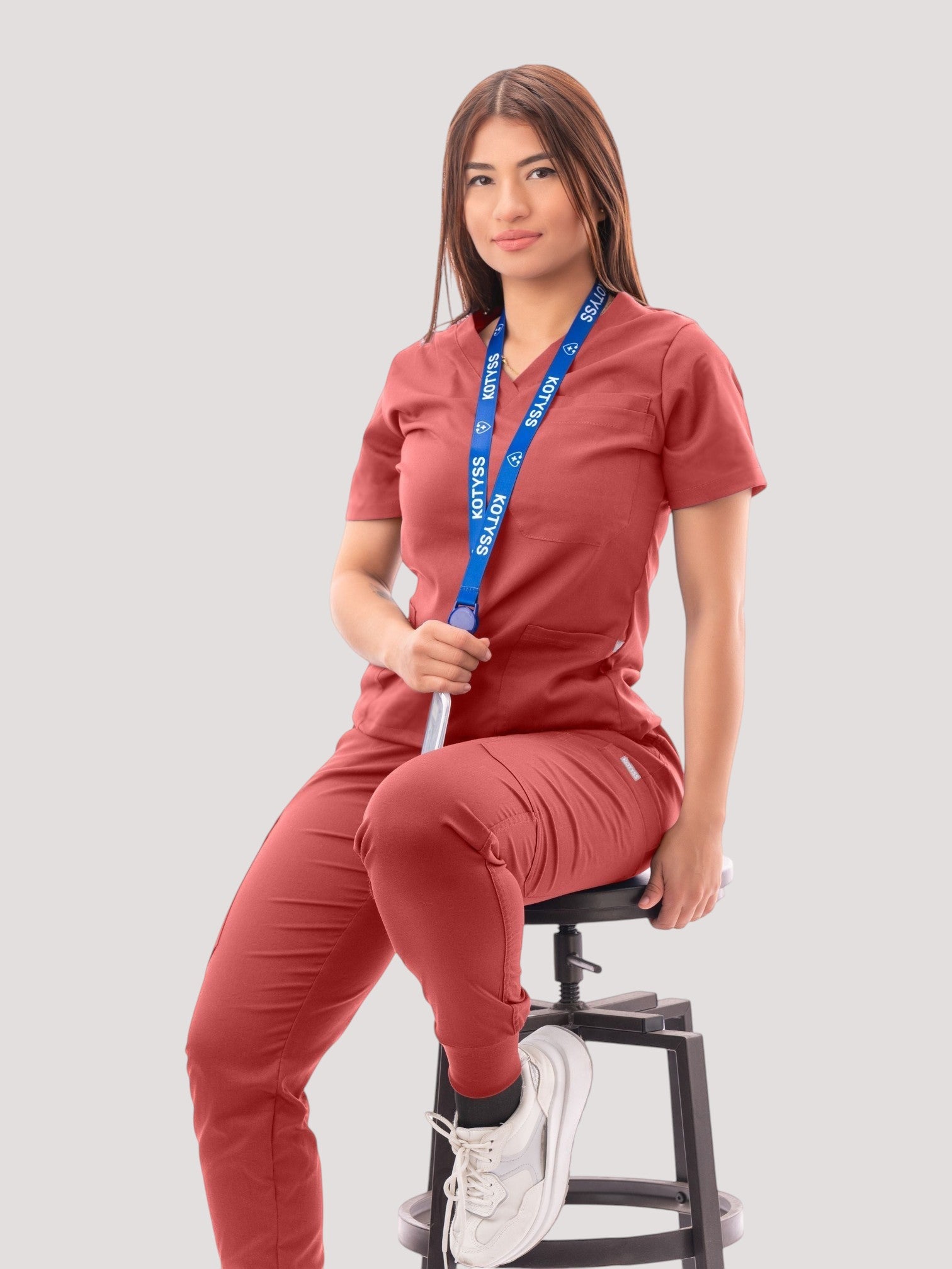 Kotyss women's rust-colored V-neck scrub top and jogger pants set with multiple pockets worn by a seated model