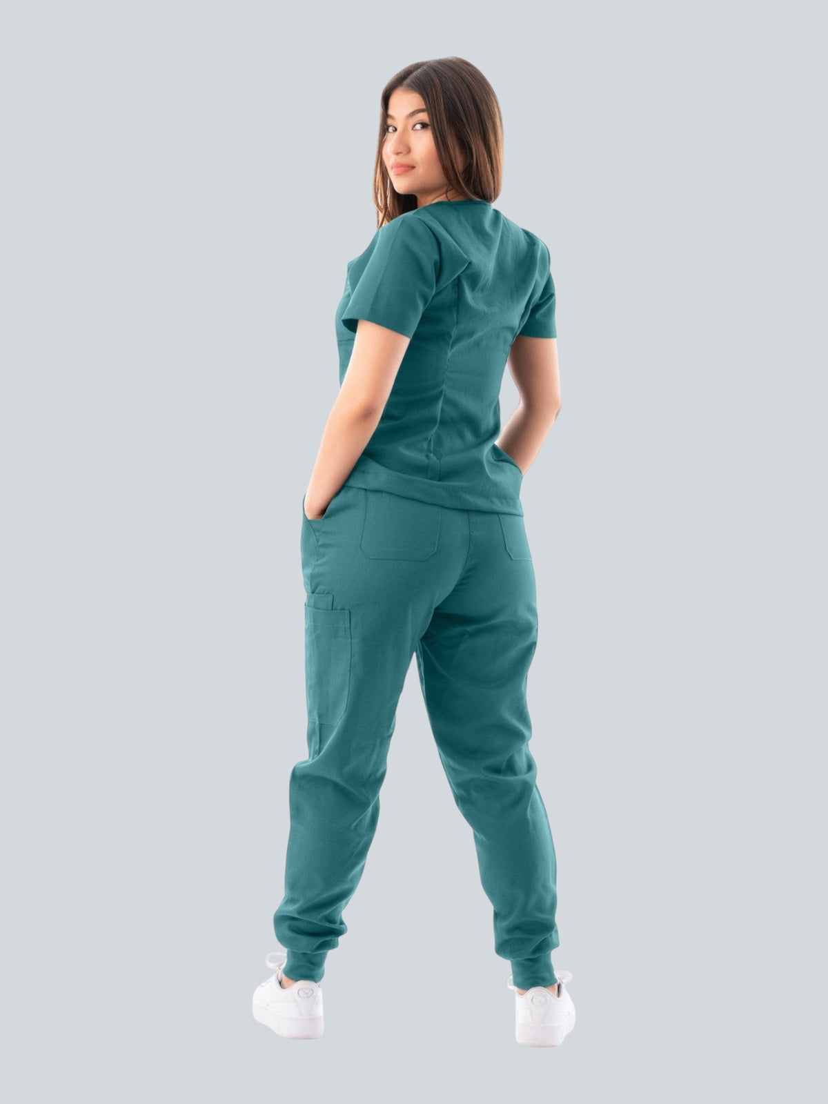 A woman wearing a teal Kotyss V-neck scrub top and jogger pants set, viewed from the back, showing multiple pockets.