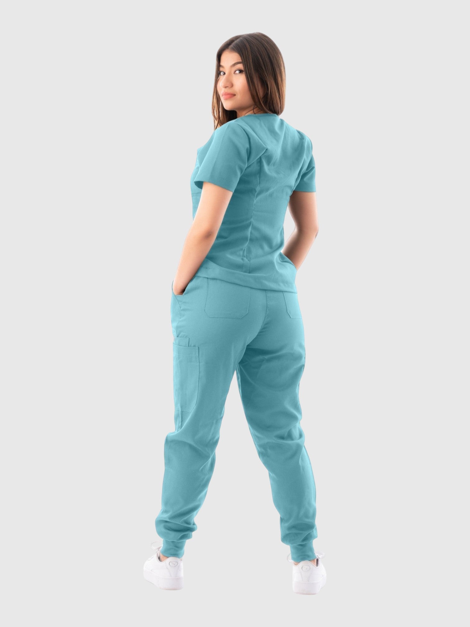 A woman wearing a Kotyss teal V-neck scrub top and matching jogger pants with multiple pockets, back view.