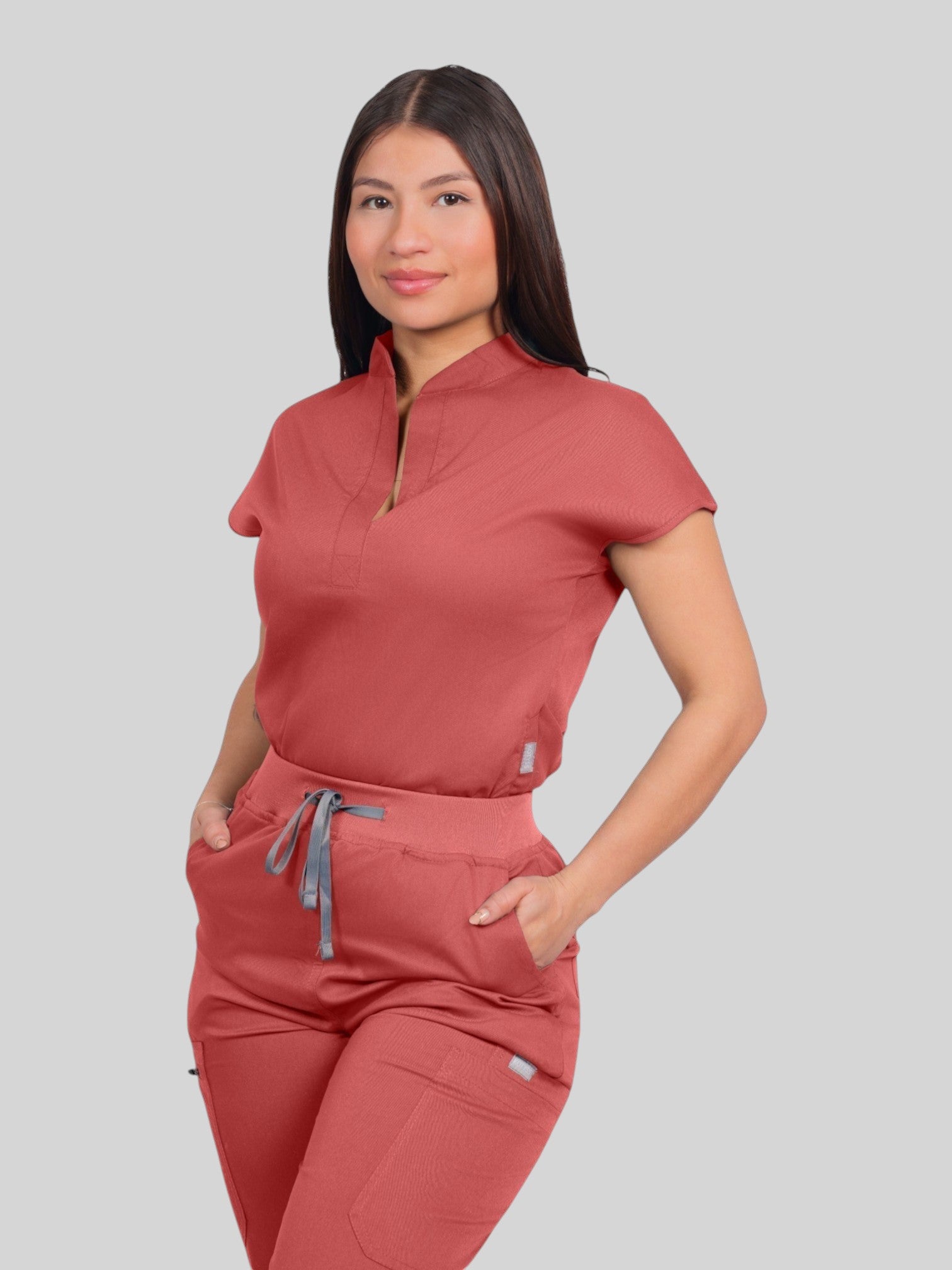 A model wearing a Kotyss terracotta collared scrub top and matching jogger pants with pockets in a studio setting.