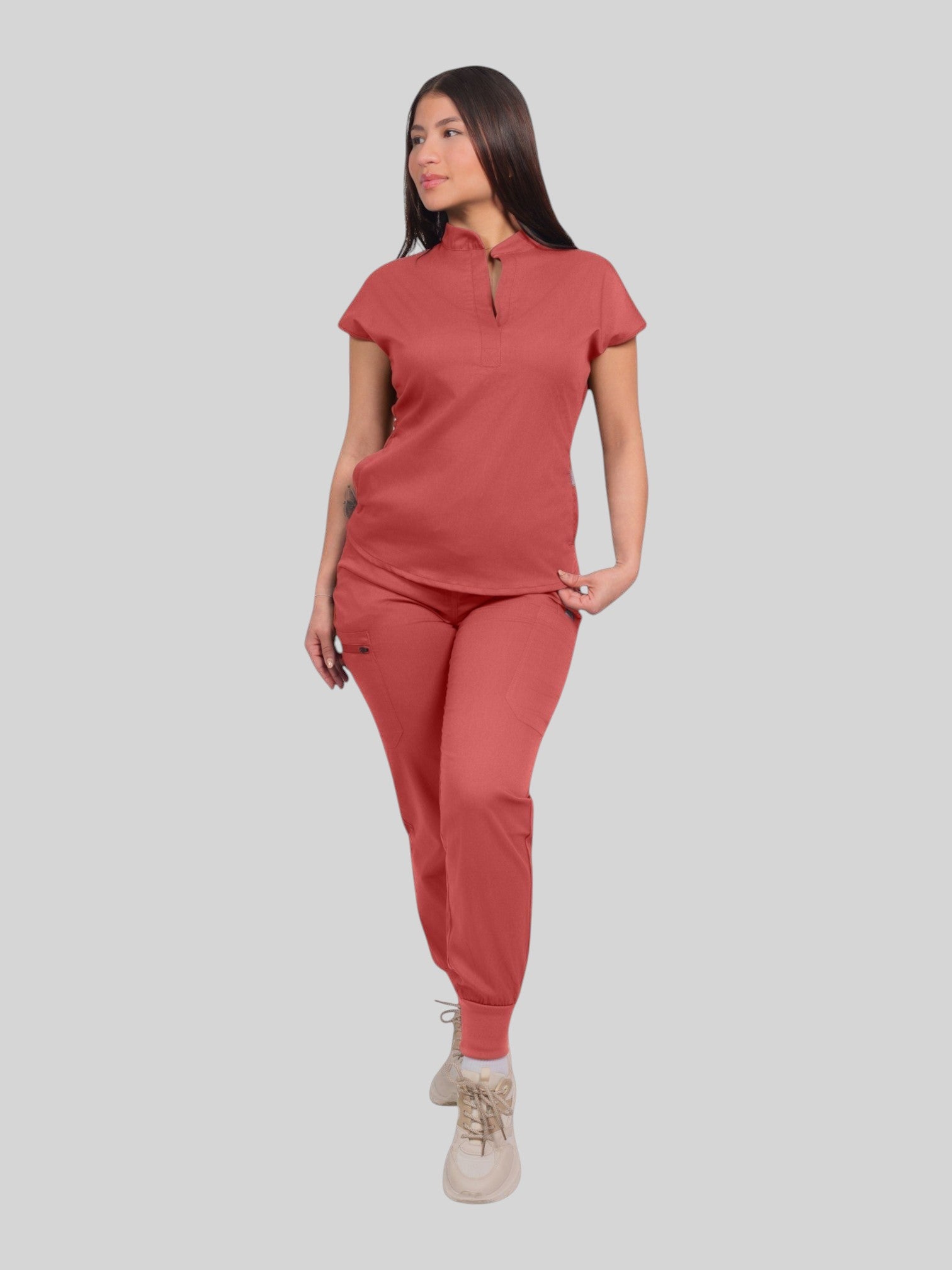 A woman wearing a Kotyss terracotta collared scrub top and matching jogger pants with multiple pockets.