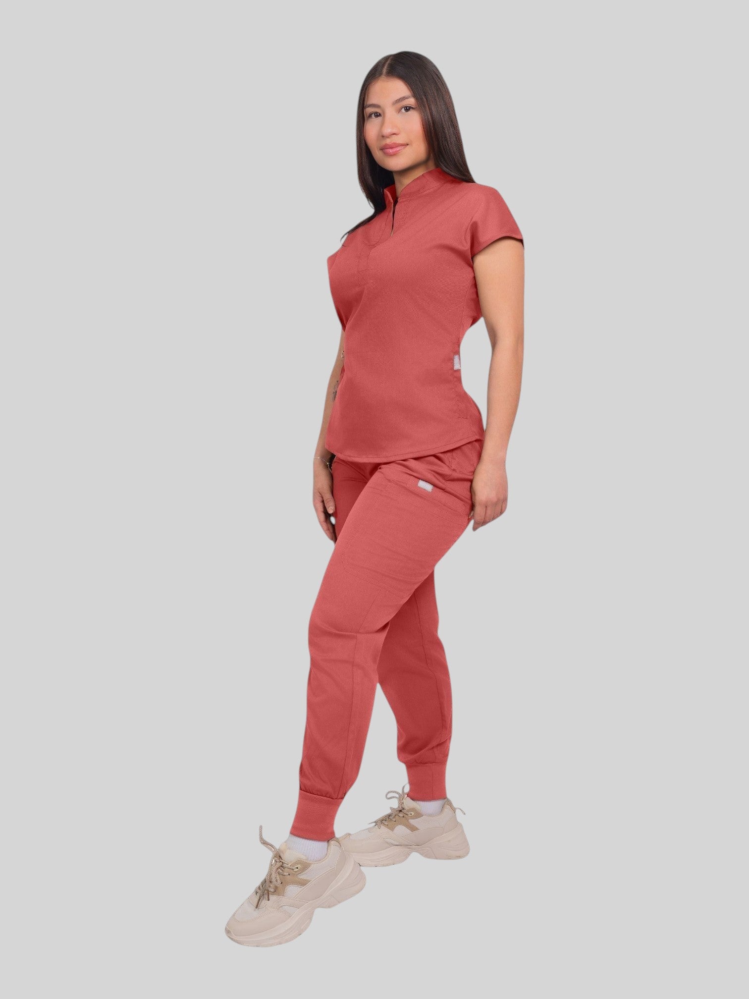 A woman wearing a Kotyss terracotta collared scrub top and matching jogger pants with multiple utility pockets.
