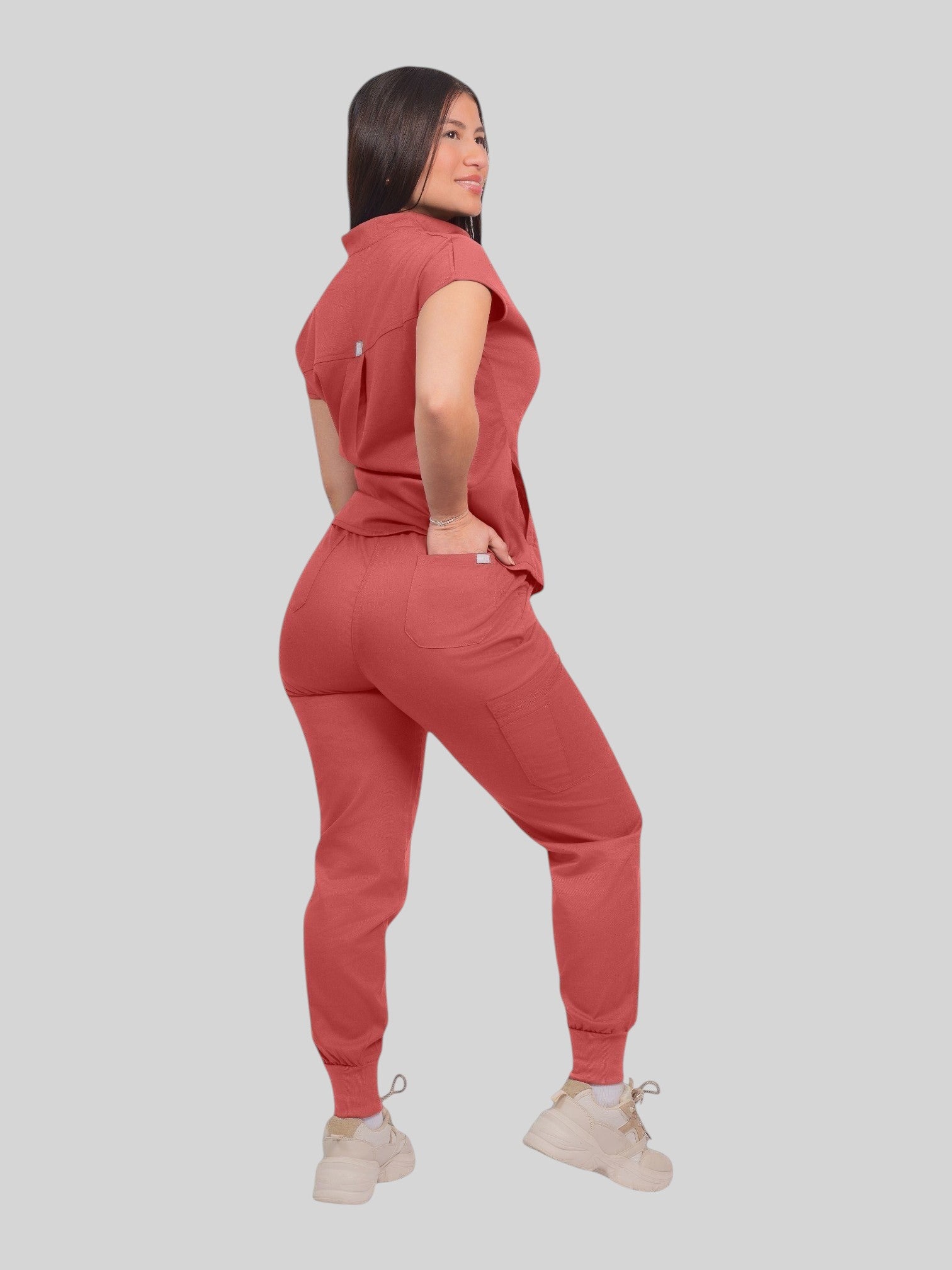 A woman wearing a Kotyss collared scrub top and matching jogger pants in a dusty rose color, back view.