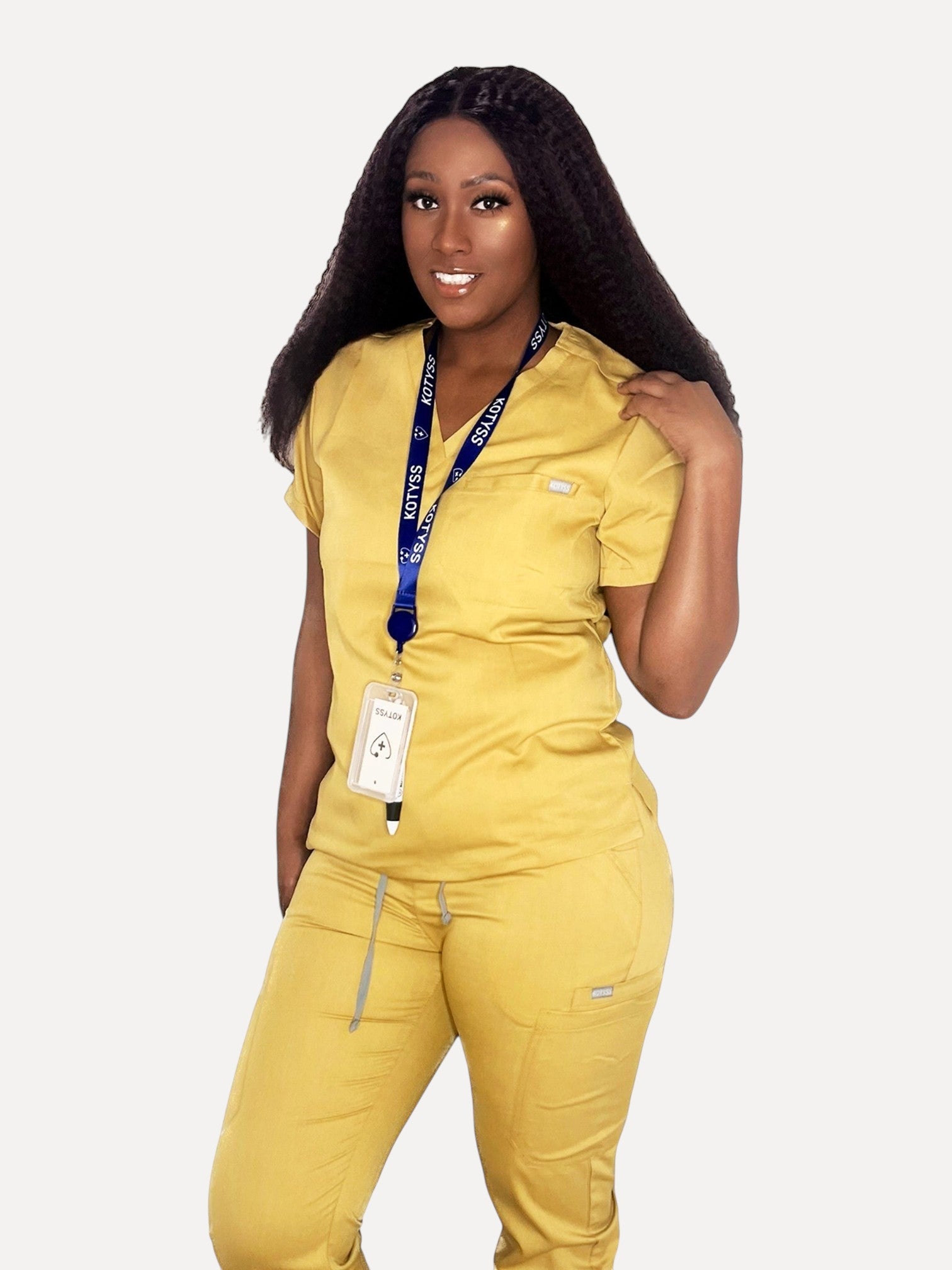 A woman wearing a yellow Kotyss V-neck scrub top and matching jogger pants with a branded lanyard.